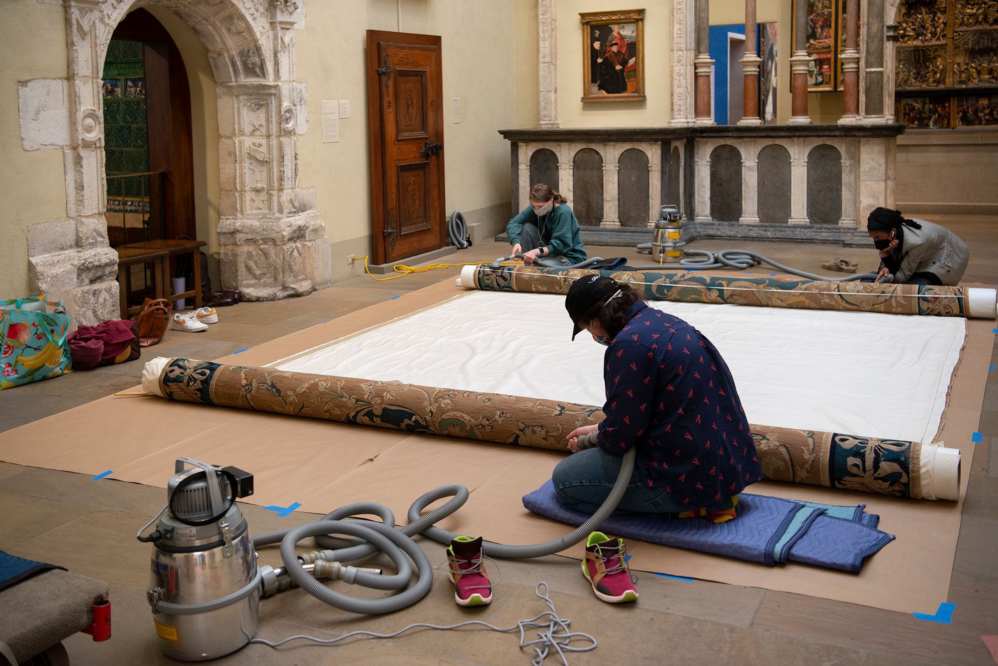 Three conservators cleaning and handling a large carpet in the European Art galleries