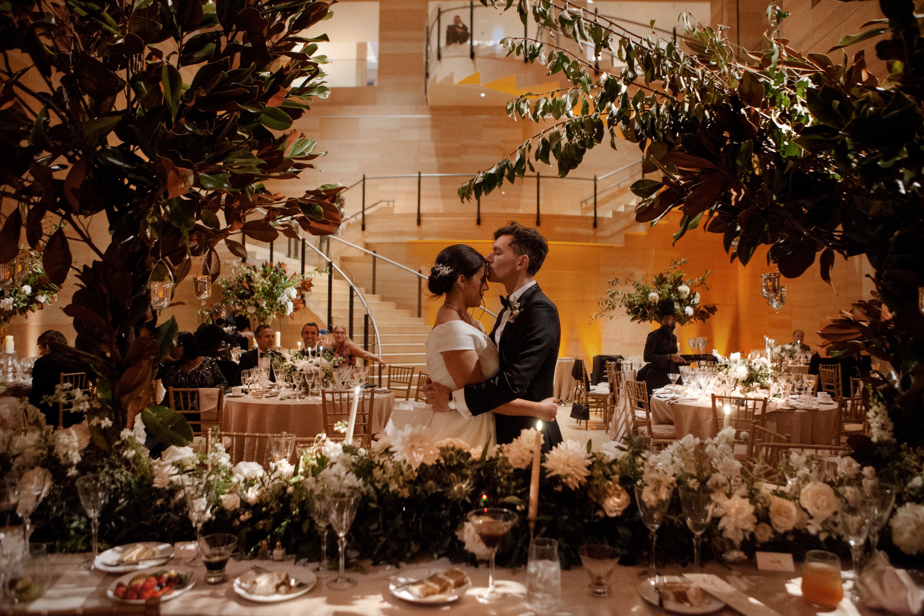 A bride a groom kissing in the Williams Forum surrounded by white flowers and wedding guests