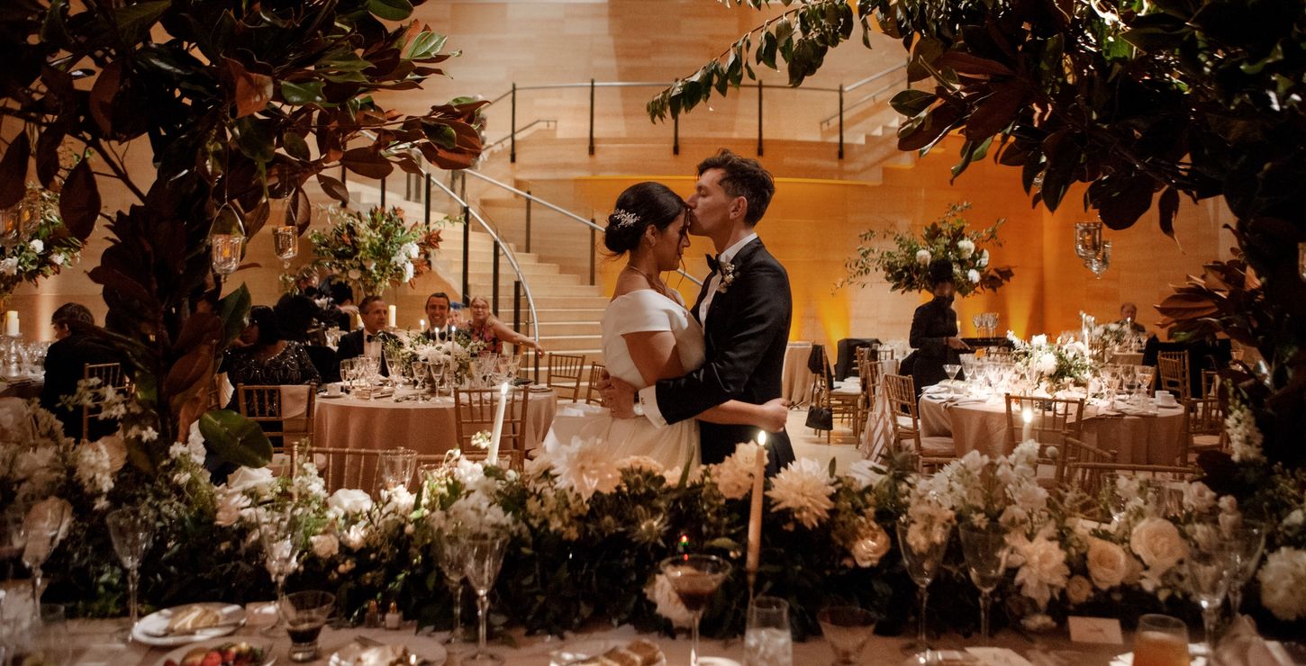 A bride a groom kissing in the Williams Forum surrounded by white flowers and wedding guests