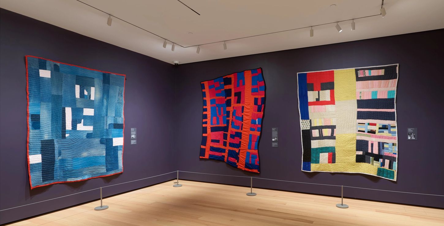 Installation view of the Gee's Bend Gallery which shows three quilts hung on the wall.