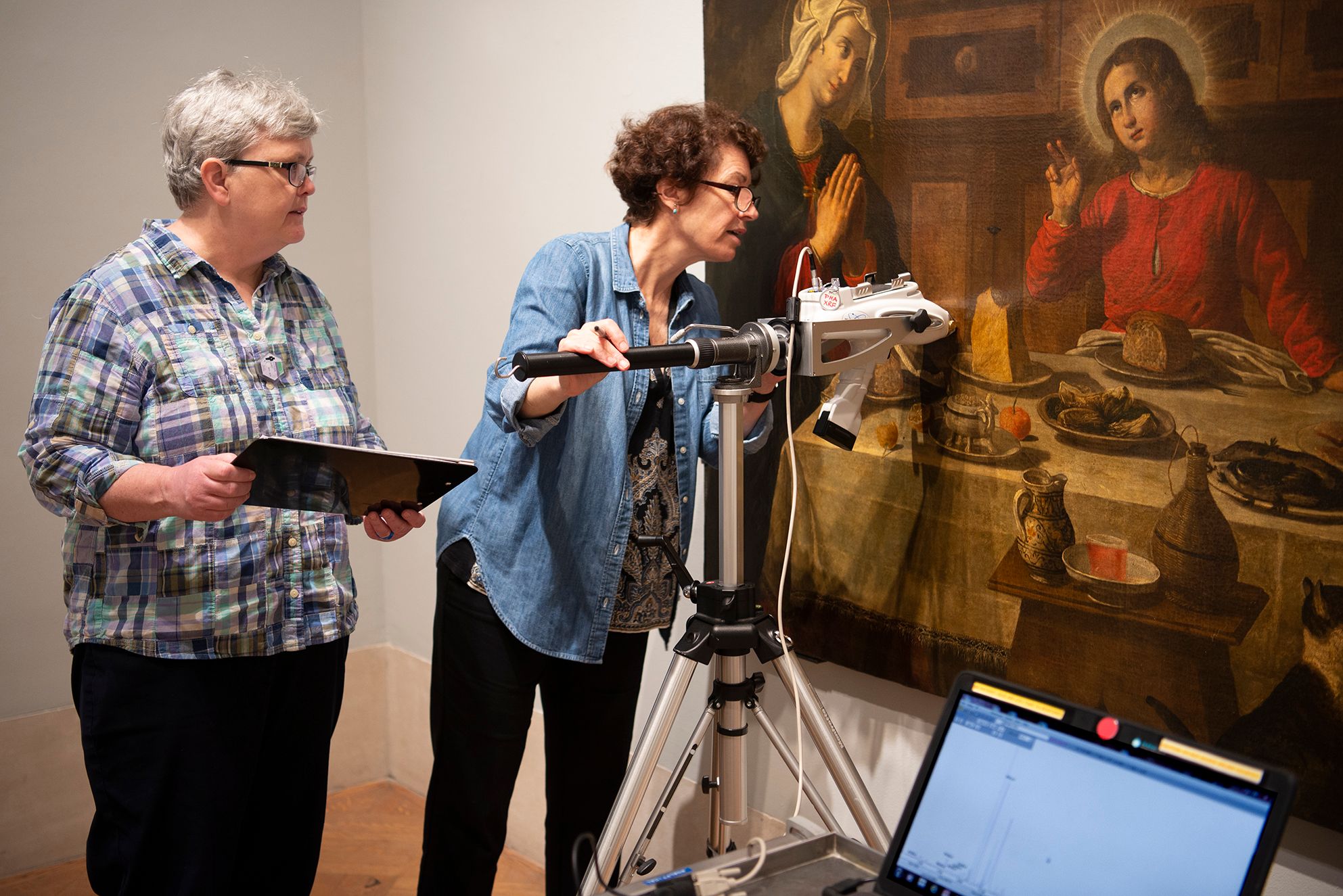 Two conservators inspecting and cleaning the European painting The Holy Family at Table
