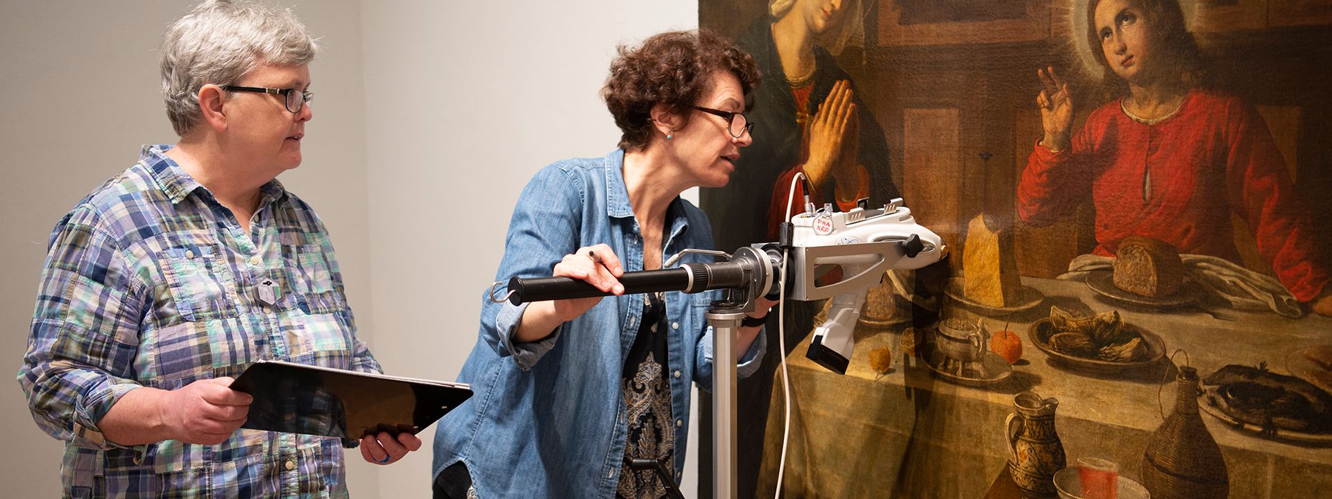 Two conservators inspecting and cleaning the European painting The Holy Family at Table
