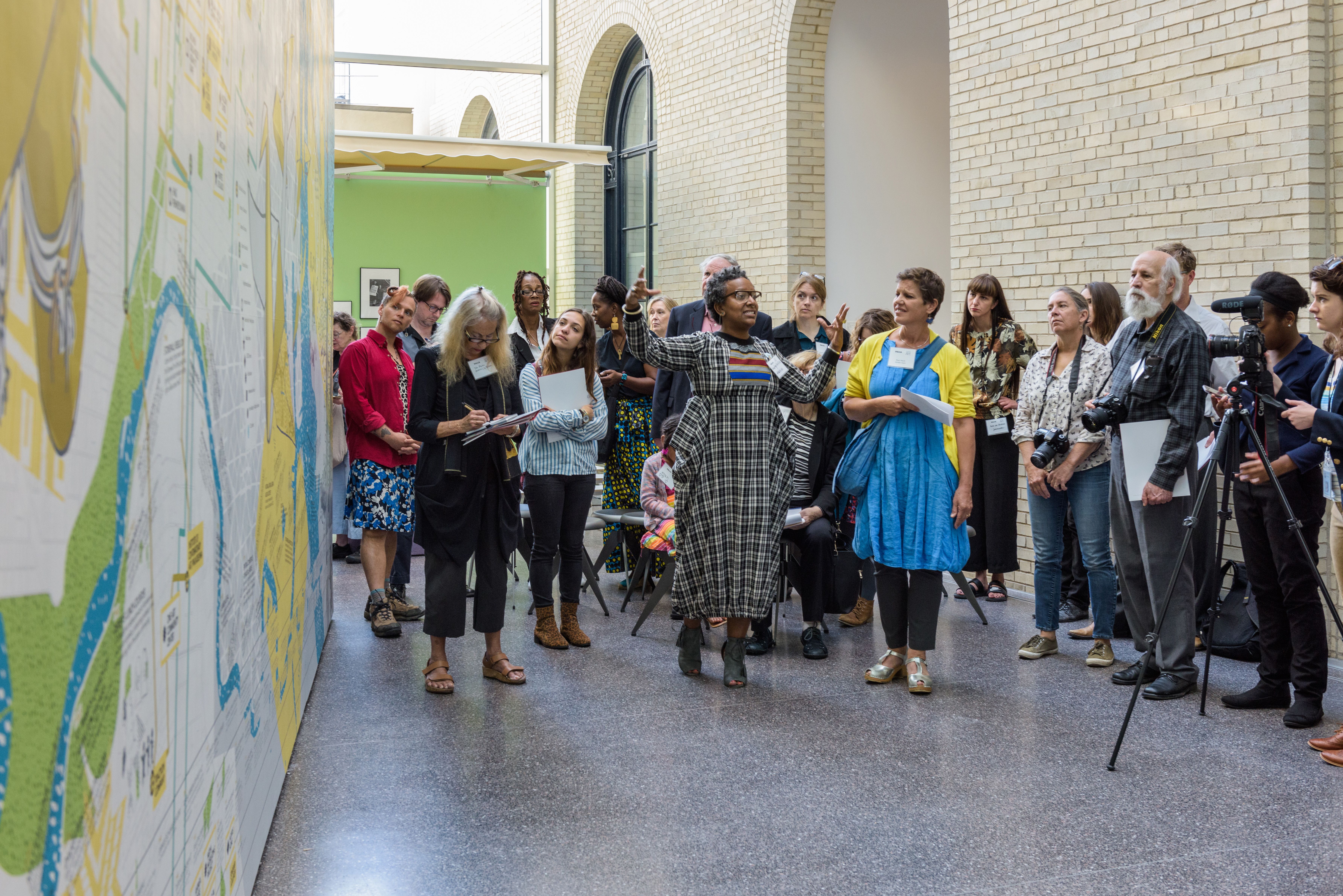 A speaker talking to a group of people about a large mural in the Perelman Building