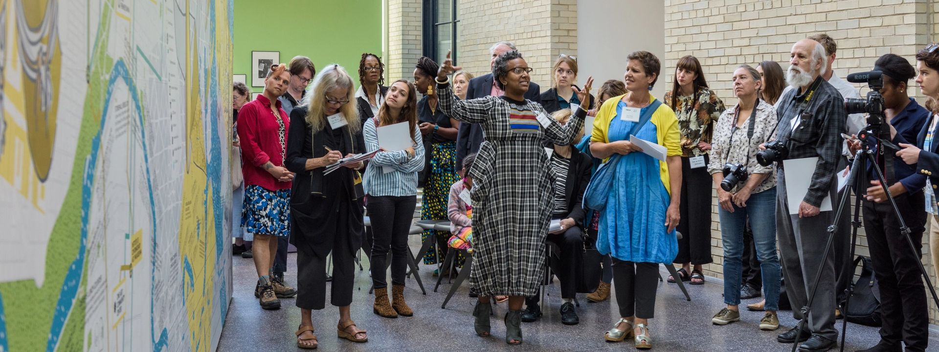 A speaker talking to a group of people about a large mural in the Perelman Building