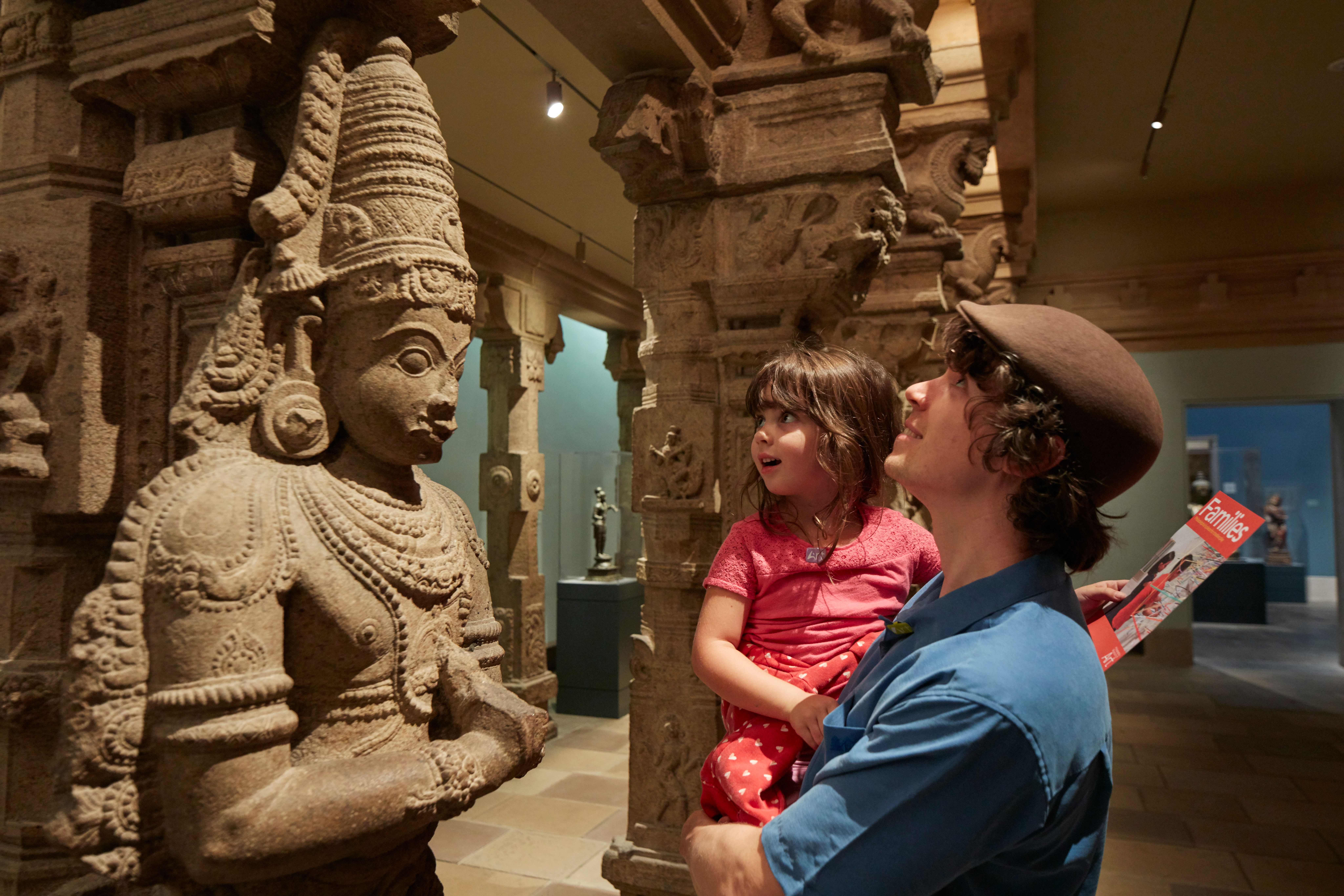 An adult holding a child up to a sculpture in the Temple Hall