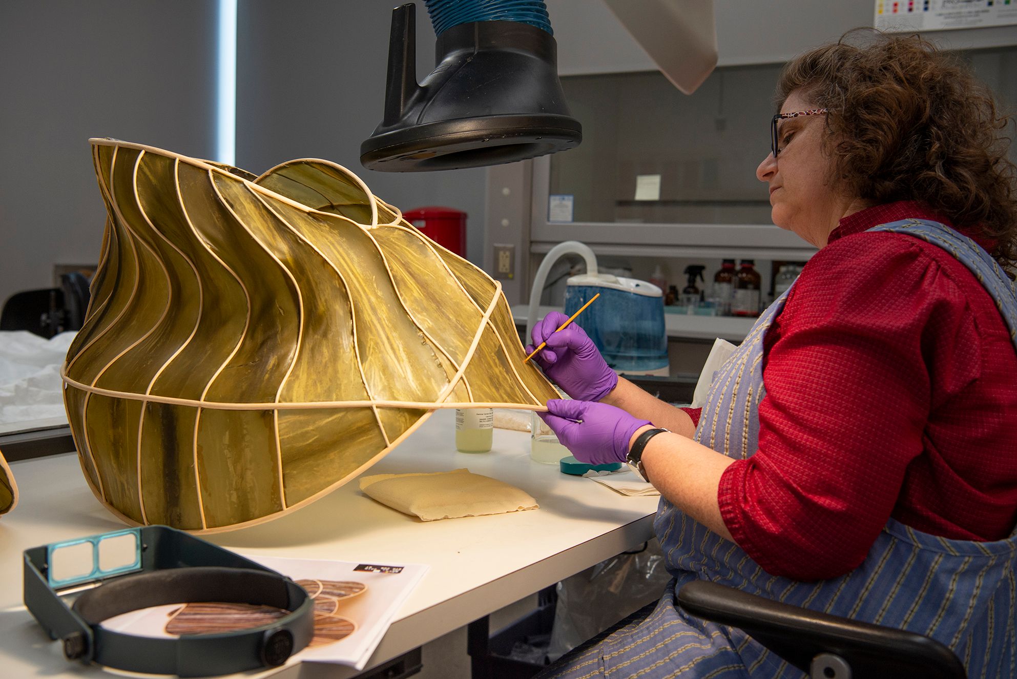 Conservator painting a large piece of a gold sculpture