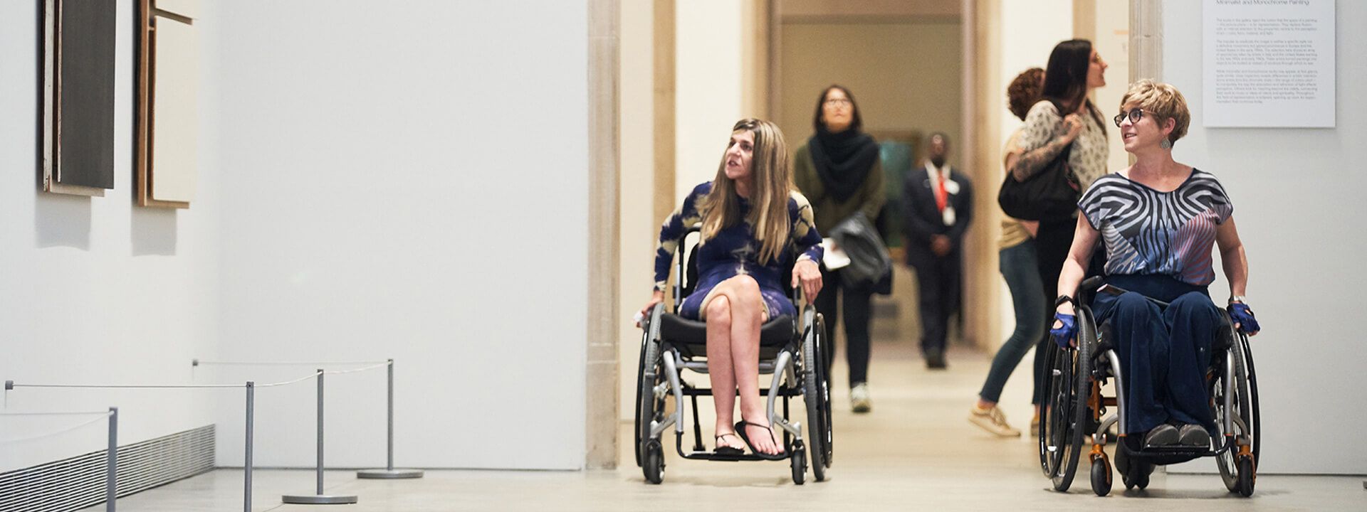 Two visitors in wheelchairs explore the galleries