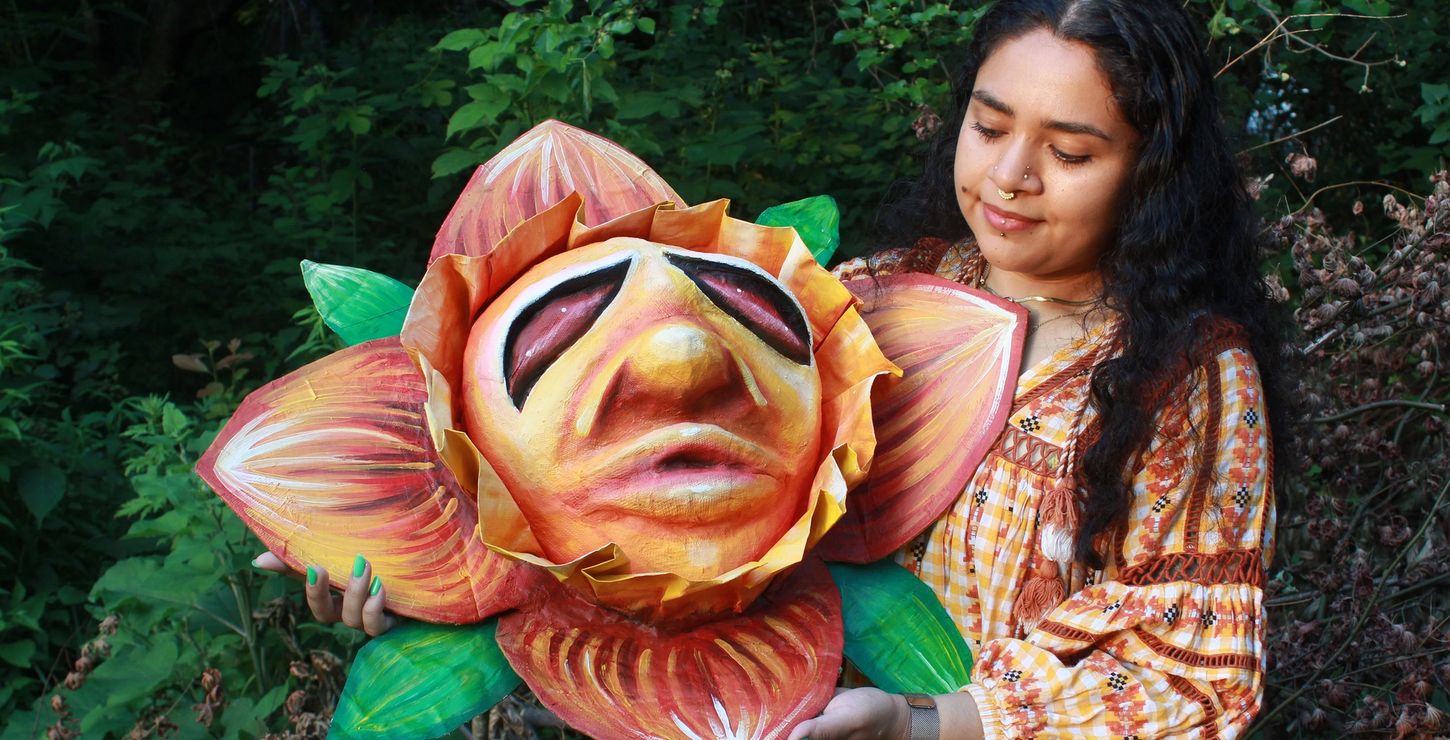 Artist Salma Garcia-Nolasco holding a large paper-mache flower head/