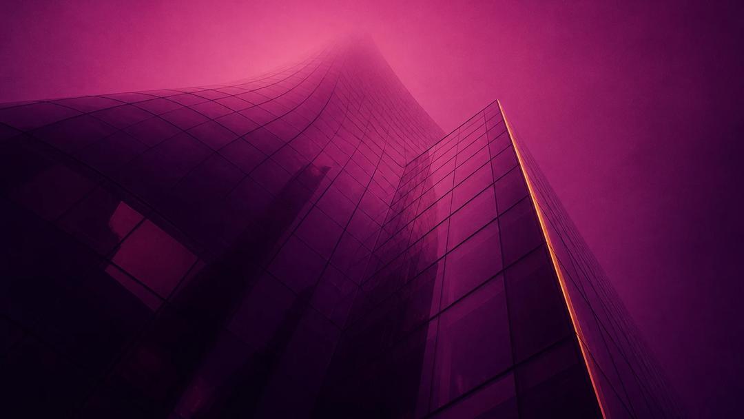 The glass facade of an office tower seen from below at dusk