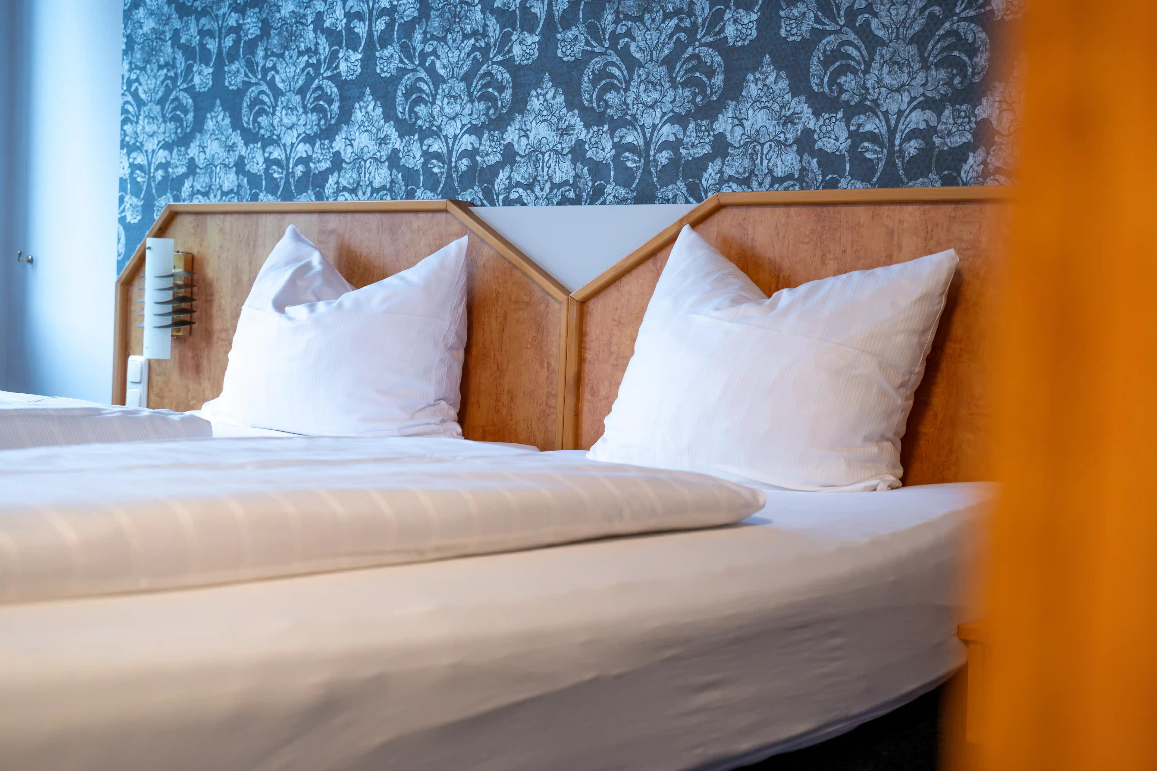 Doppelbett mit weißer Bettwäsche vor blau gemusterter Wand