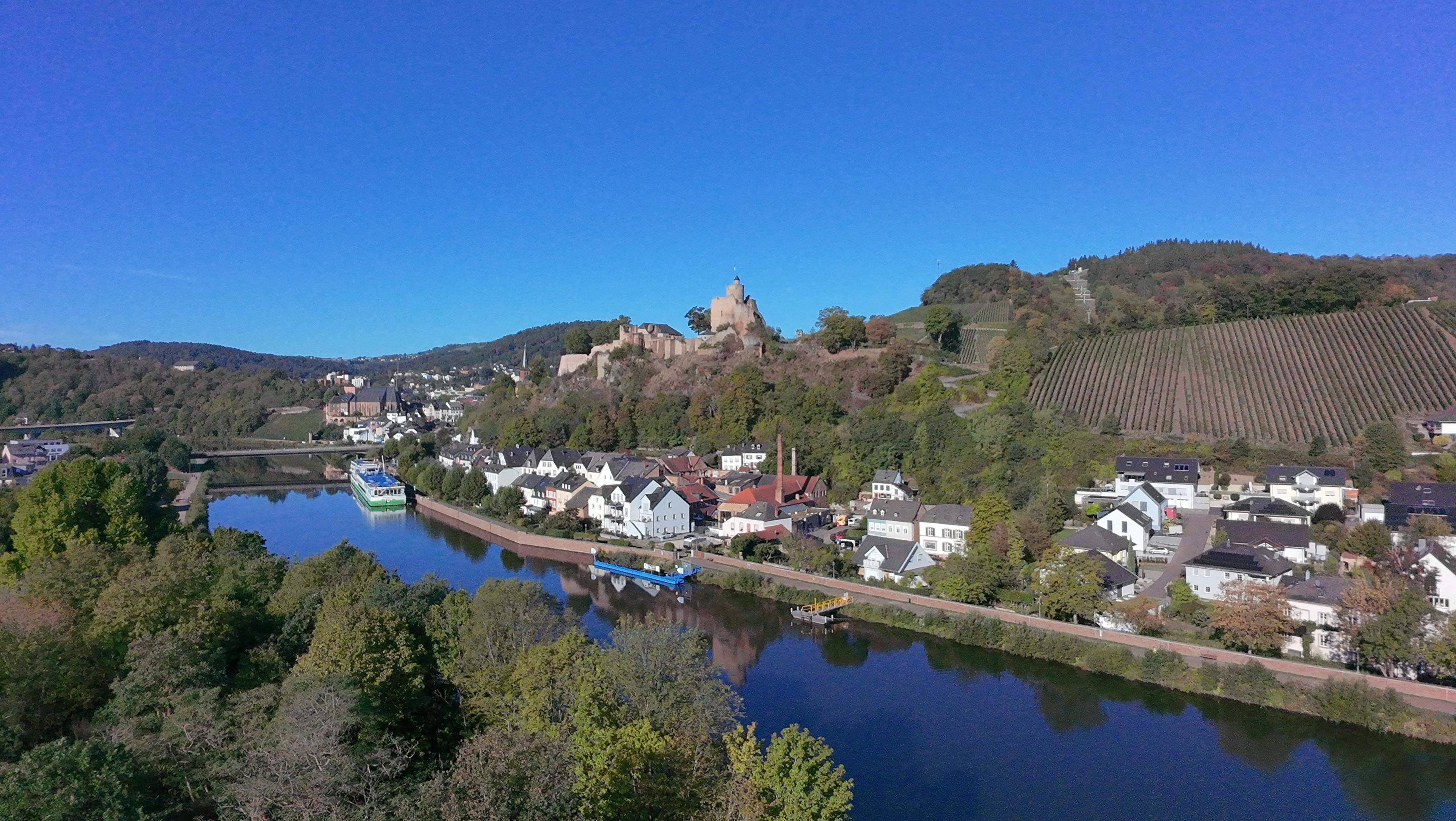 Luftaufnahme der Saar bei Saarburg mit einem Schiff am Ufer, darüber die Burg und ein Weinberg
