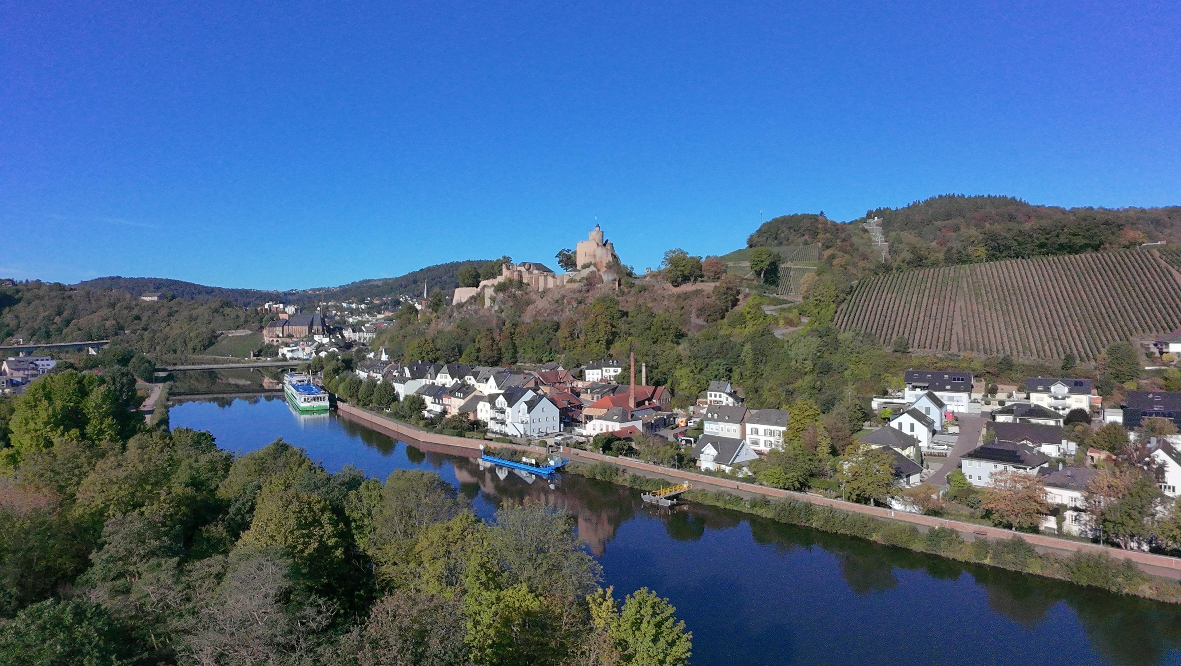 Luftaufnahme der Saar bei Saarburg mit einem Schiff am Ufer, darüber die Burg und ein Weinberg