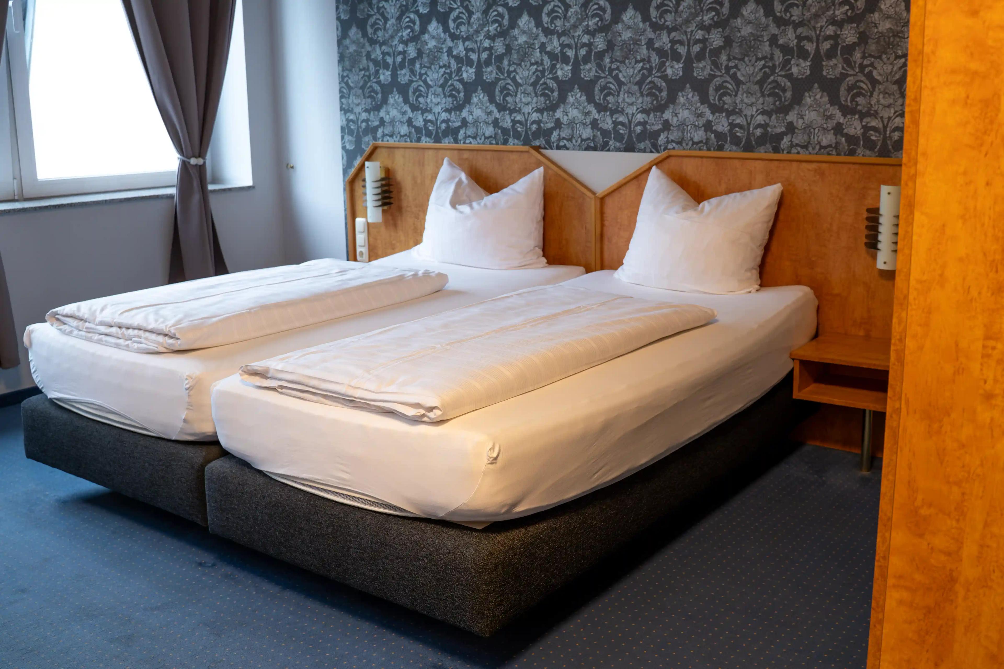 Standard-Doppelzimmer mit breitem Bett, gemusterter Tapete und blauem Teppich
