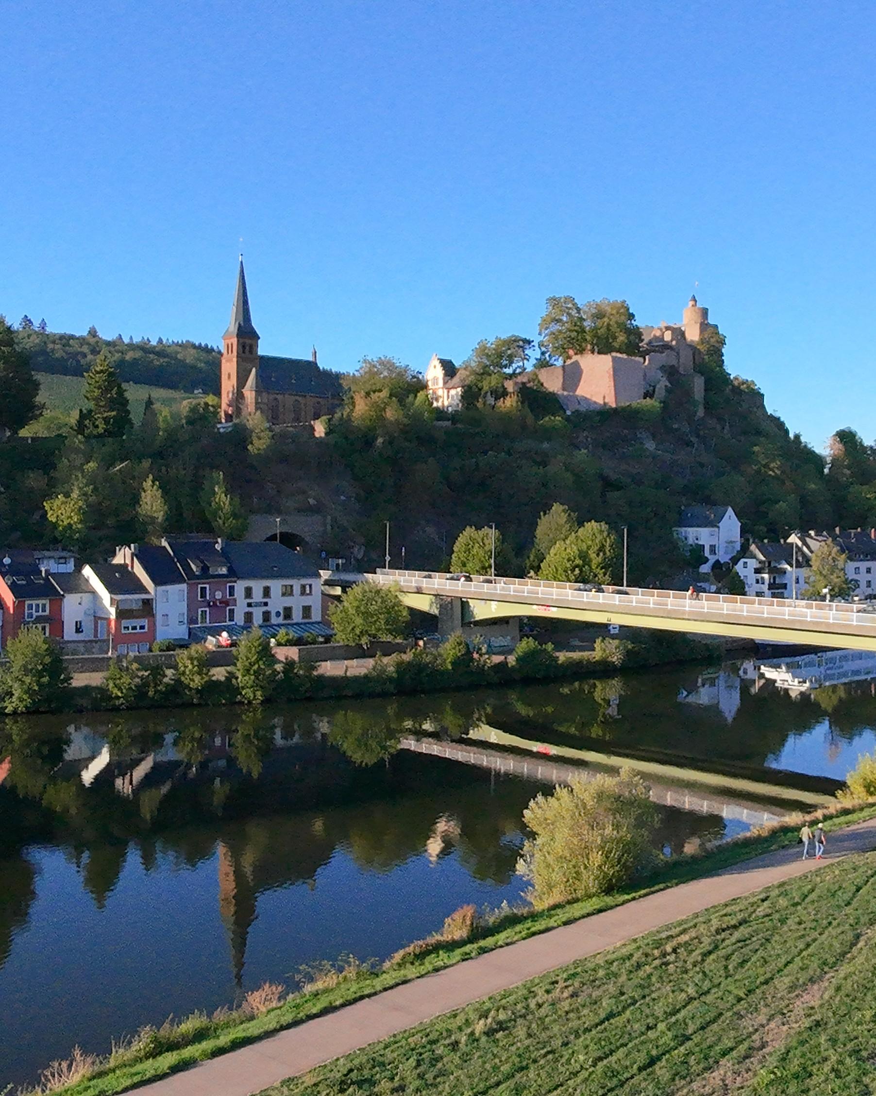 Uferweg an der Saar mit Blick auf die Saarburger Altstadt, die Brücke, einen Kirchturm und die Burg
