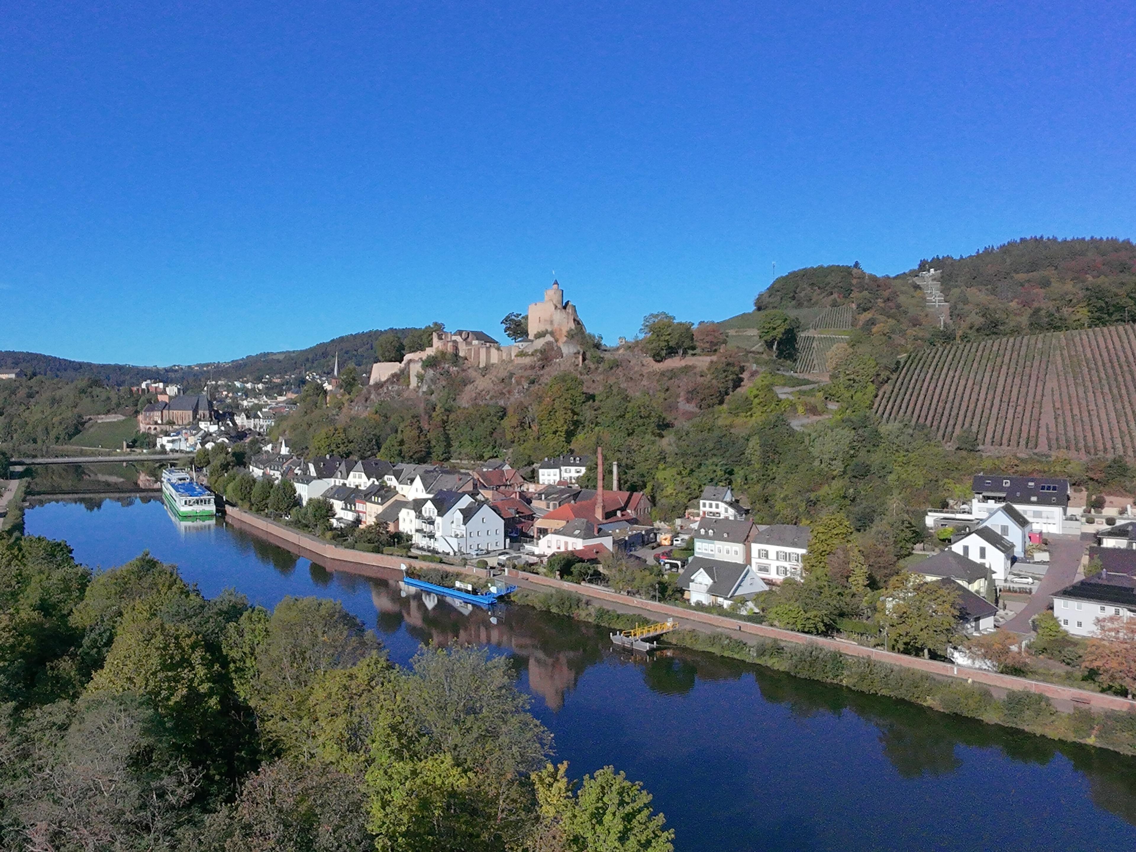Luftaufnahme der Burg Saarburg über der Saar mit Schiffen am Ufer und einem Weinberg am Hang