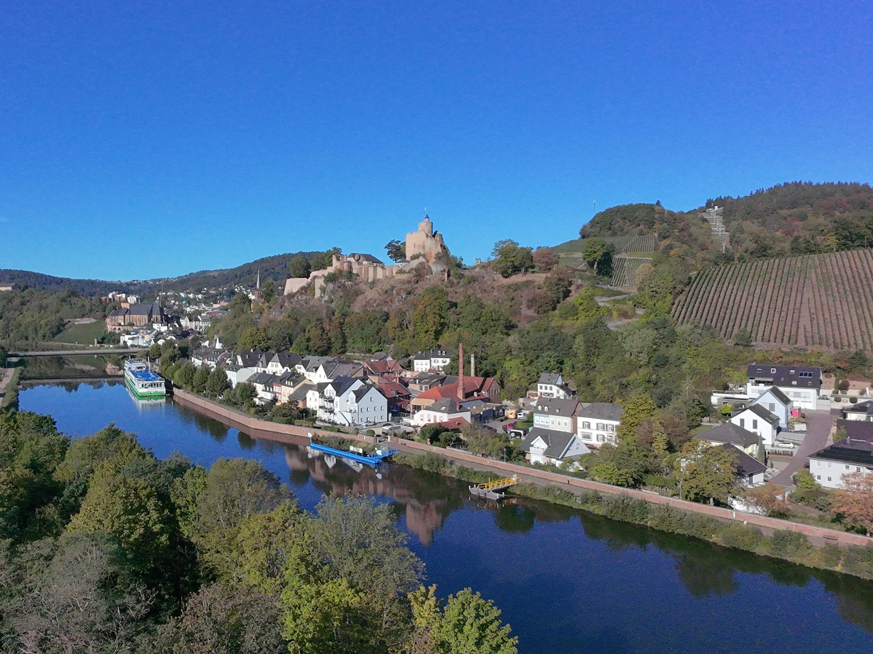 Luftaufnahme der Burg Saarburg über der Saar mit Schiffen am Ufer und einem Weinberg am Hang