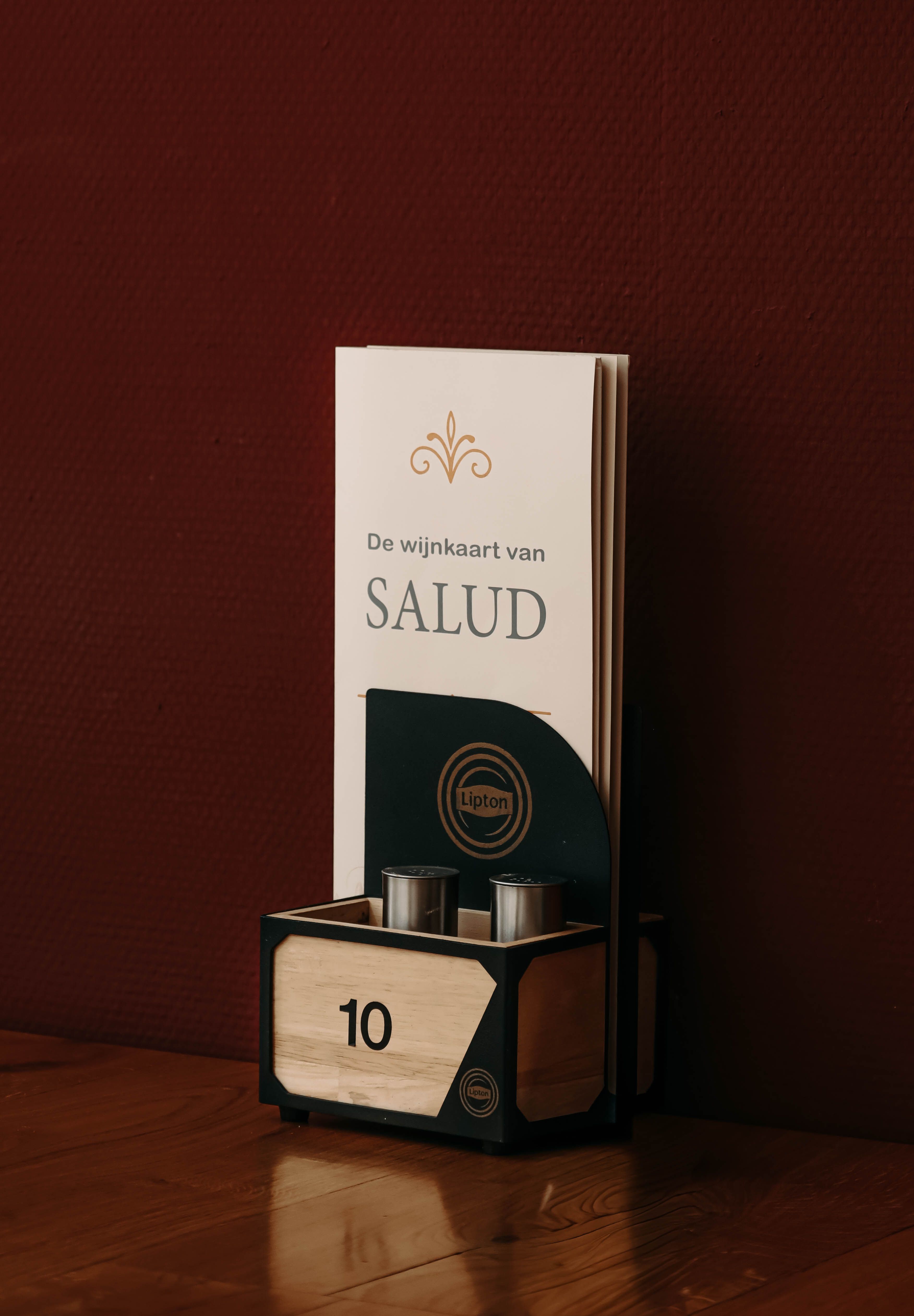 De wijnkaart van Grand Cafe Salud op een tafel tegen een donkerrode muur