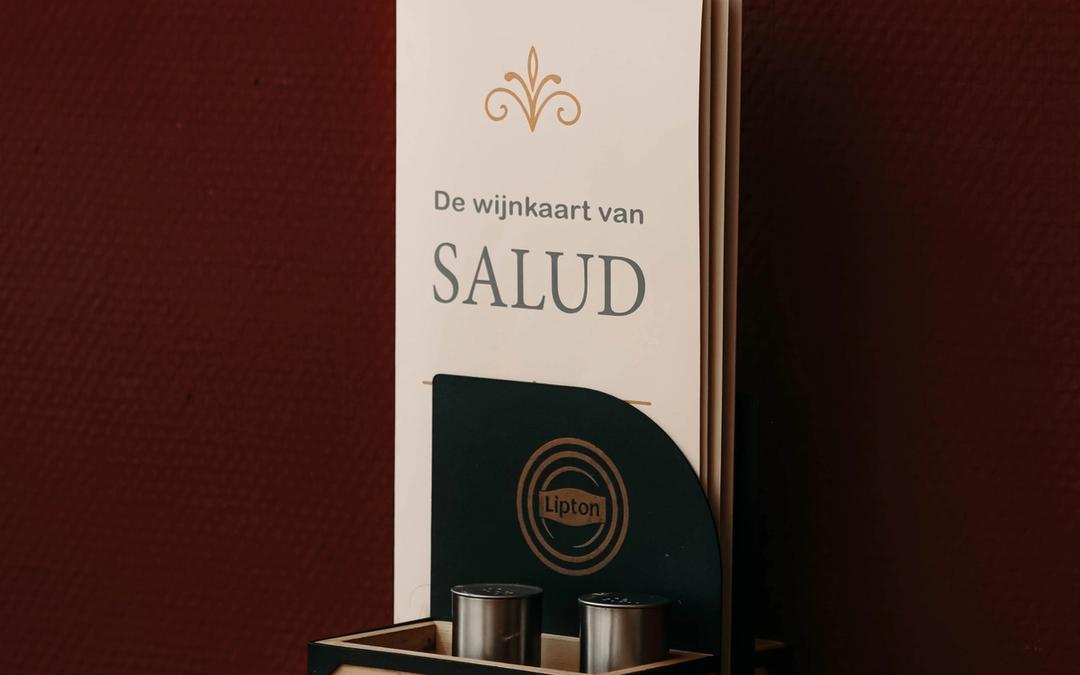 De wijnkaart van Grand Cafe Salud op een tafel tegen een donkerrode muur