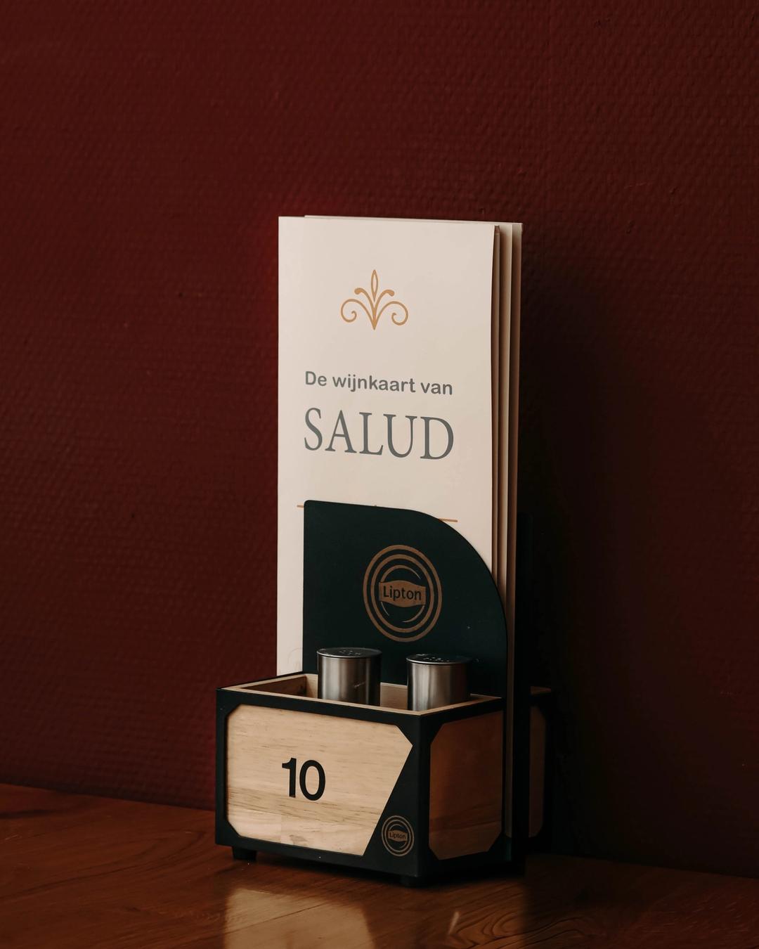 De wijnkaart van Grand Cafe Salud op een tafel tegen een donkerrode muur