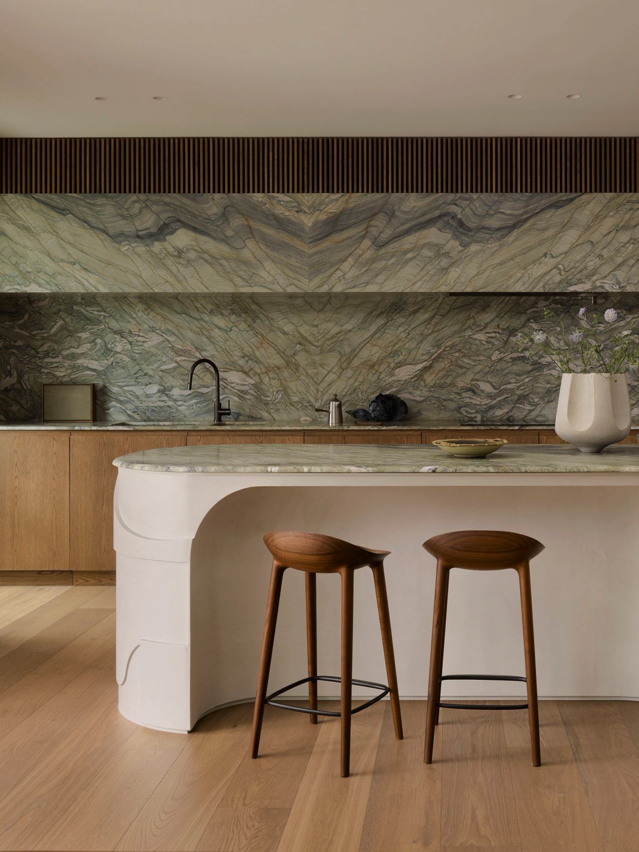Dancing on the Ceiling Dancing On The Ceiling Sculptural white plaster kitchen island with a book-matched marble top, paired with two dark wood bar stools, set against a dramatic mirrored marble splashback and oak cabinetry