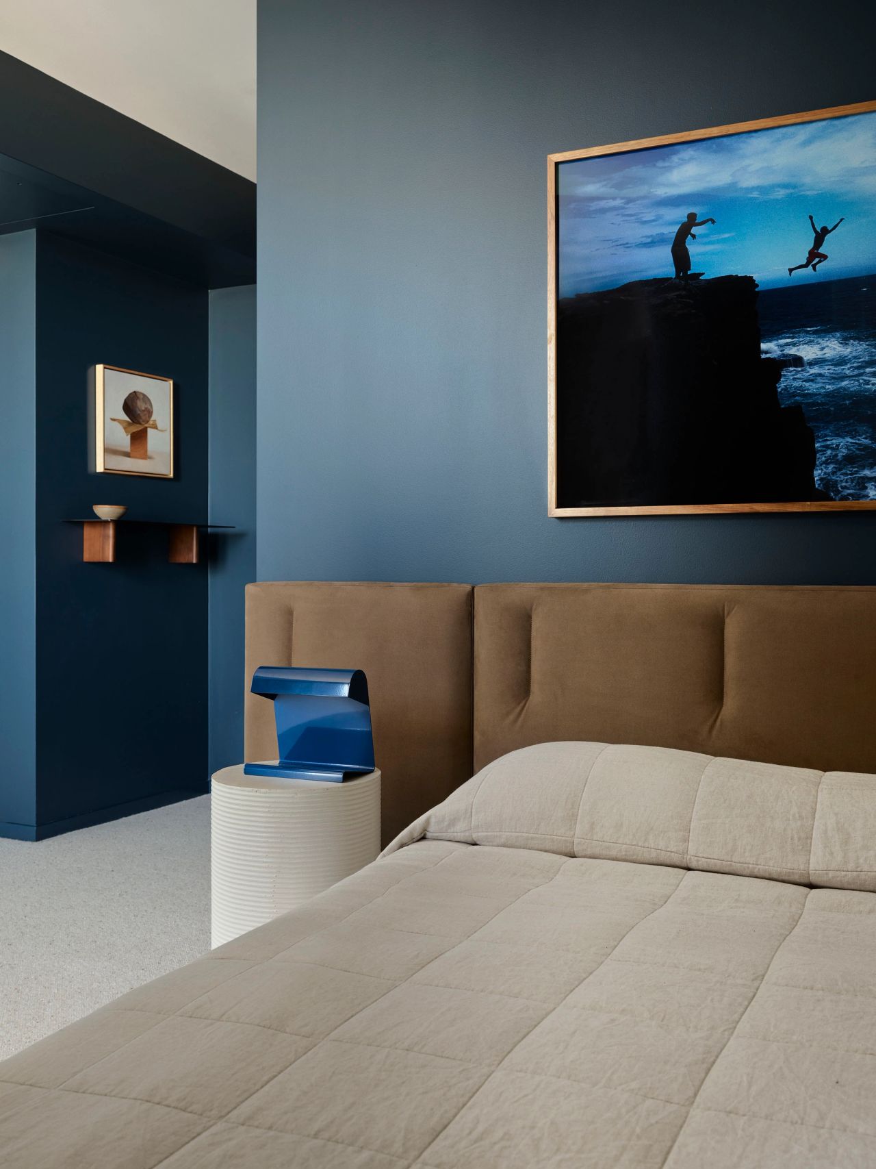Deep ocean-blue walls frame a bespoke upholstered bed, sculptural lighting and evocative coastal photography.