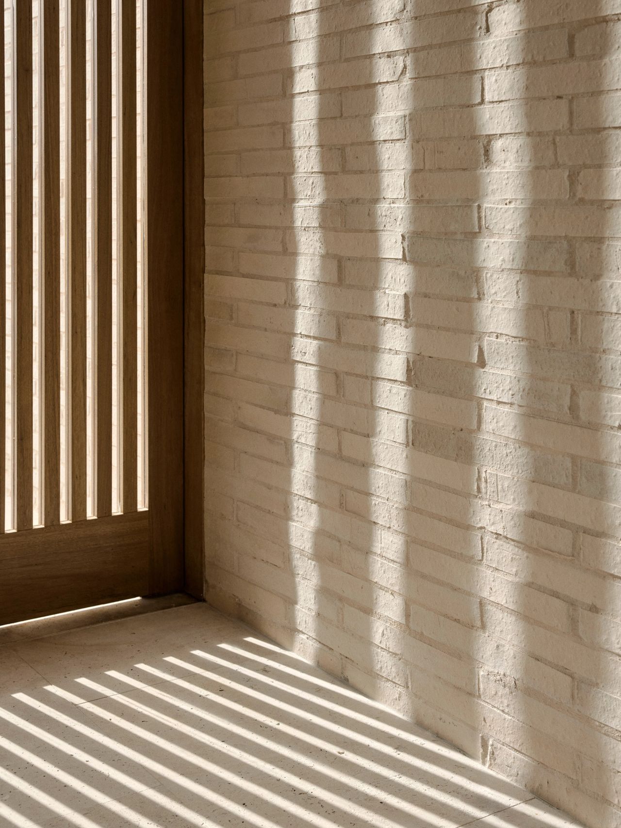 Sunset Whitewashed brick wall with striped shadow patterns cast by a wooden slatted screen or door, in warm afternoon light