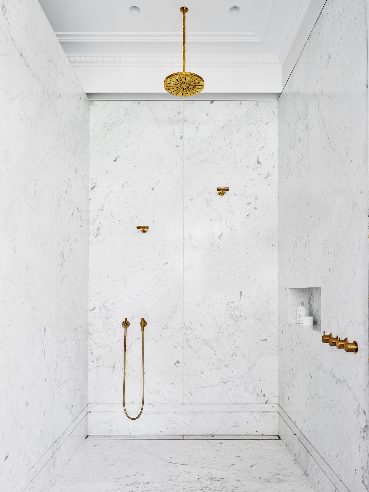 Luxurious walk-in shower clad in white marble with a statement brass rainfall shower head and matching brass fixtures.