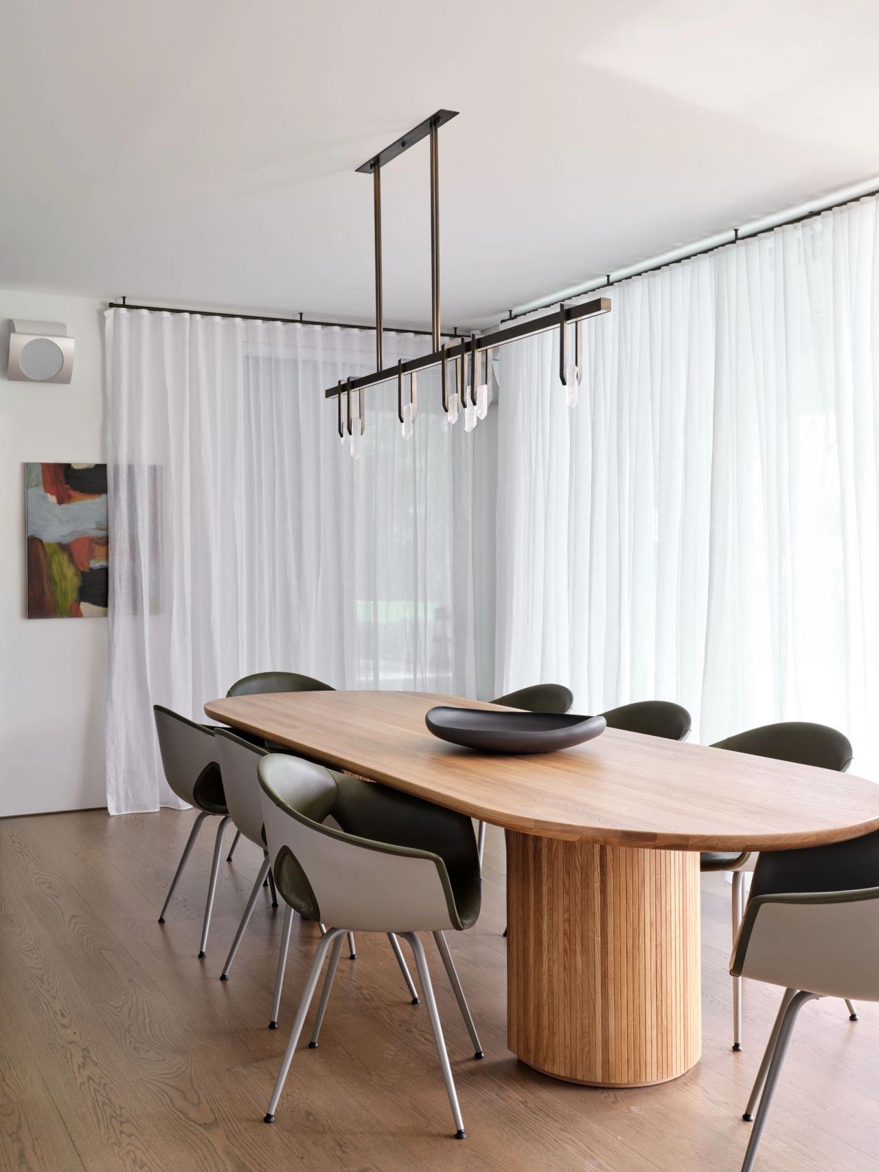 Contemporary dining room with sculptural timber table, dark upholstered chairs and linear pendant lighting.