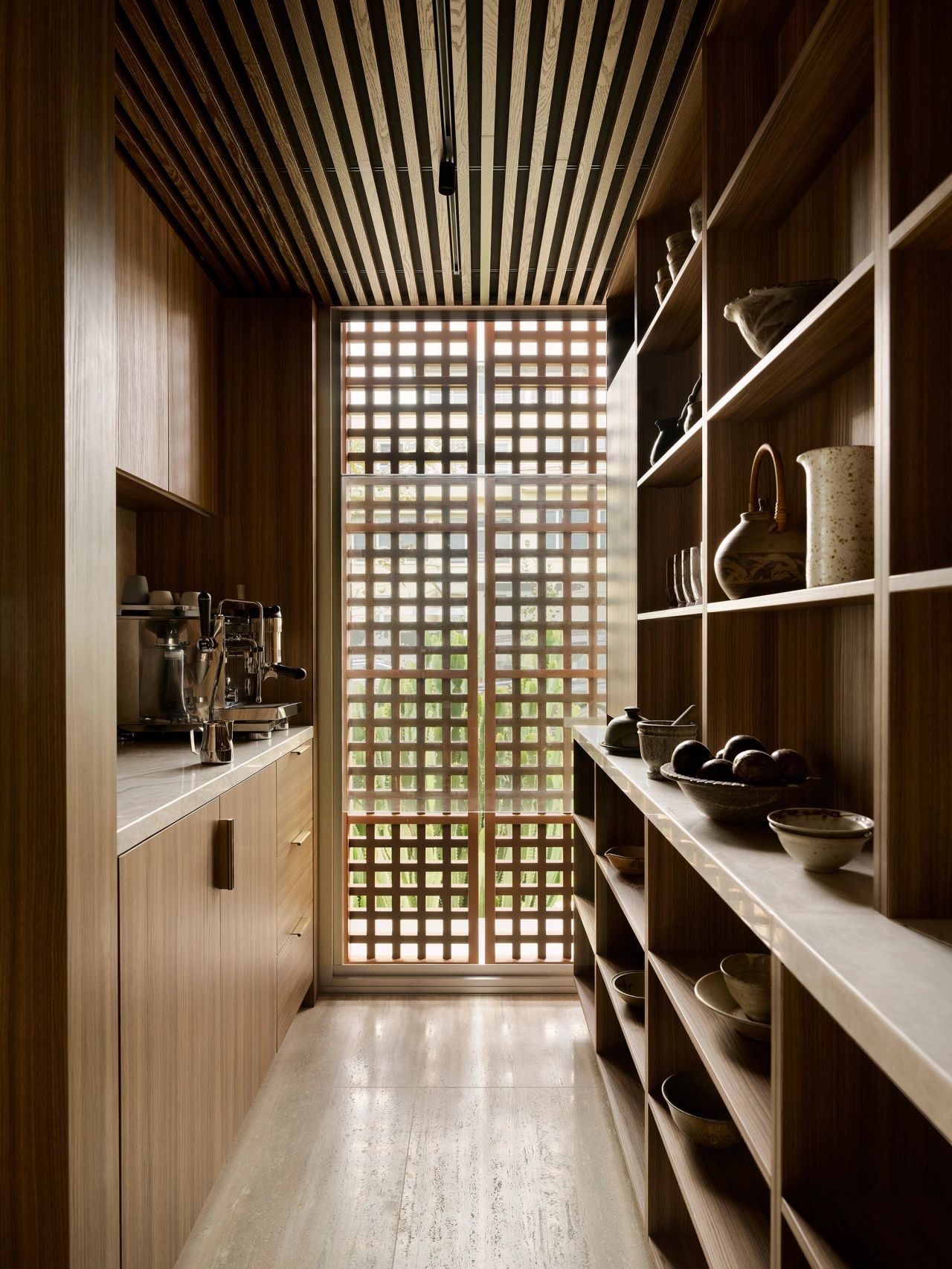 Orla contemporary butler's pantry with Brazilian-influenced dark timber joinery and shelving, styled with ceramics and glassware, looking through to a timber lattice facade and timber batten ceiling detail.
