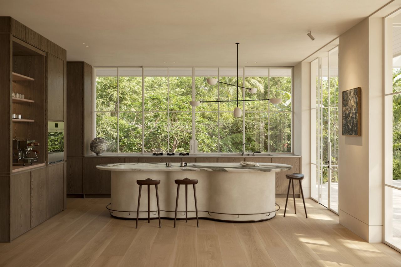 Lady M Kitchen with a sculptural curved marble island and timber bar stools beneath a branching pendant light, dark timber cabinetry with integrated appliances, and full-height windows overlooking lush garden greenery