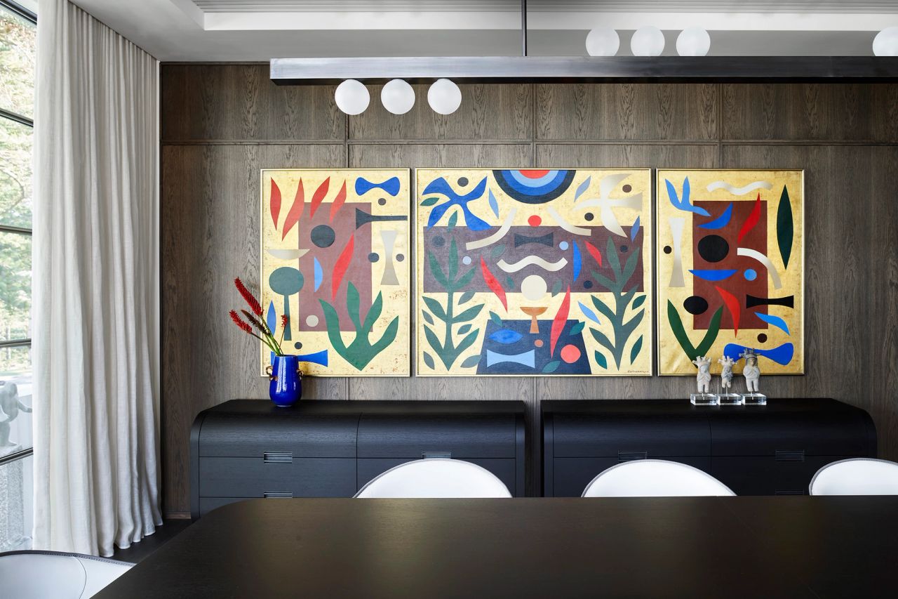 Contemporary dining room with dark timber wall panelling, a colourful abstract triptych, black curved sideboards and a sculptural linear pendant.