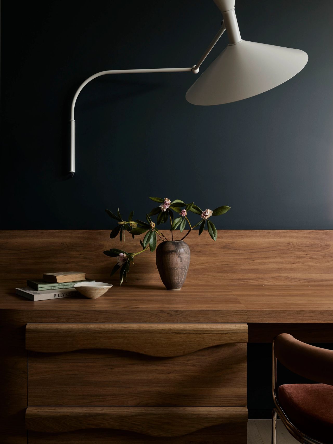 Patchwork Dark wood open shelving styled with stacked coffee-table books, a small black bowl, a textured burgundy vase, and ceramic accents.