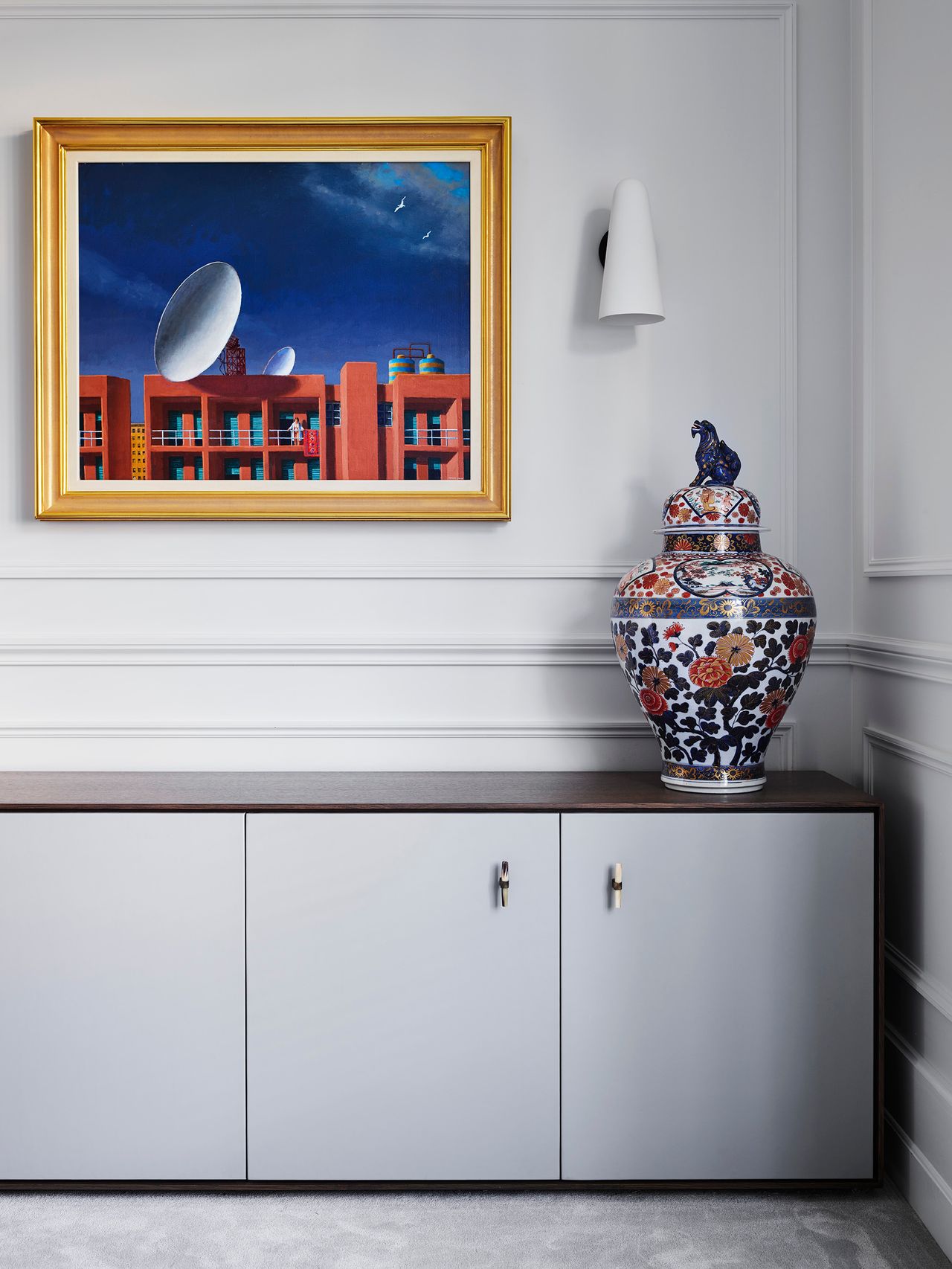 A vibrant gold-framed artwork and intricately patterned ceramic urn bring colour and character to a refined interior with crisp white cabinetry and traditional wall panelling.