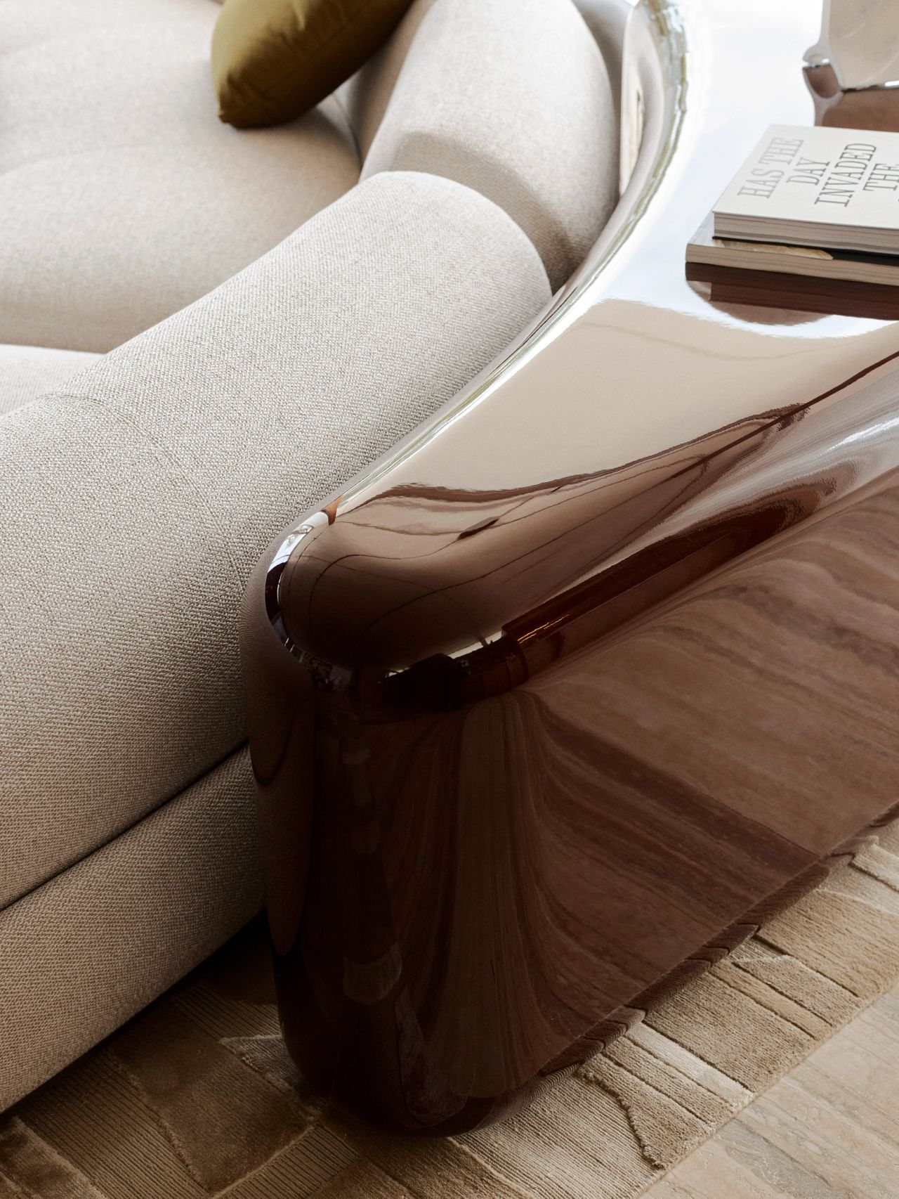 Orla contemporary living room blending Brazilian influences. Detail of a cream curved modular lounge sits on a geometric-patterned rug, with a wine coloured high-gloss table behind it
