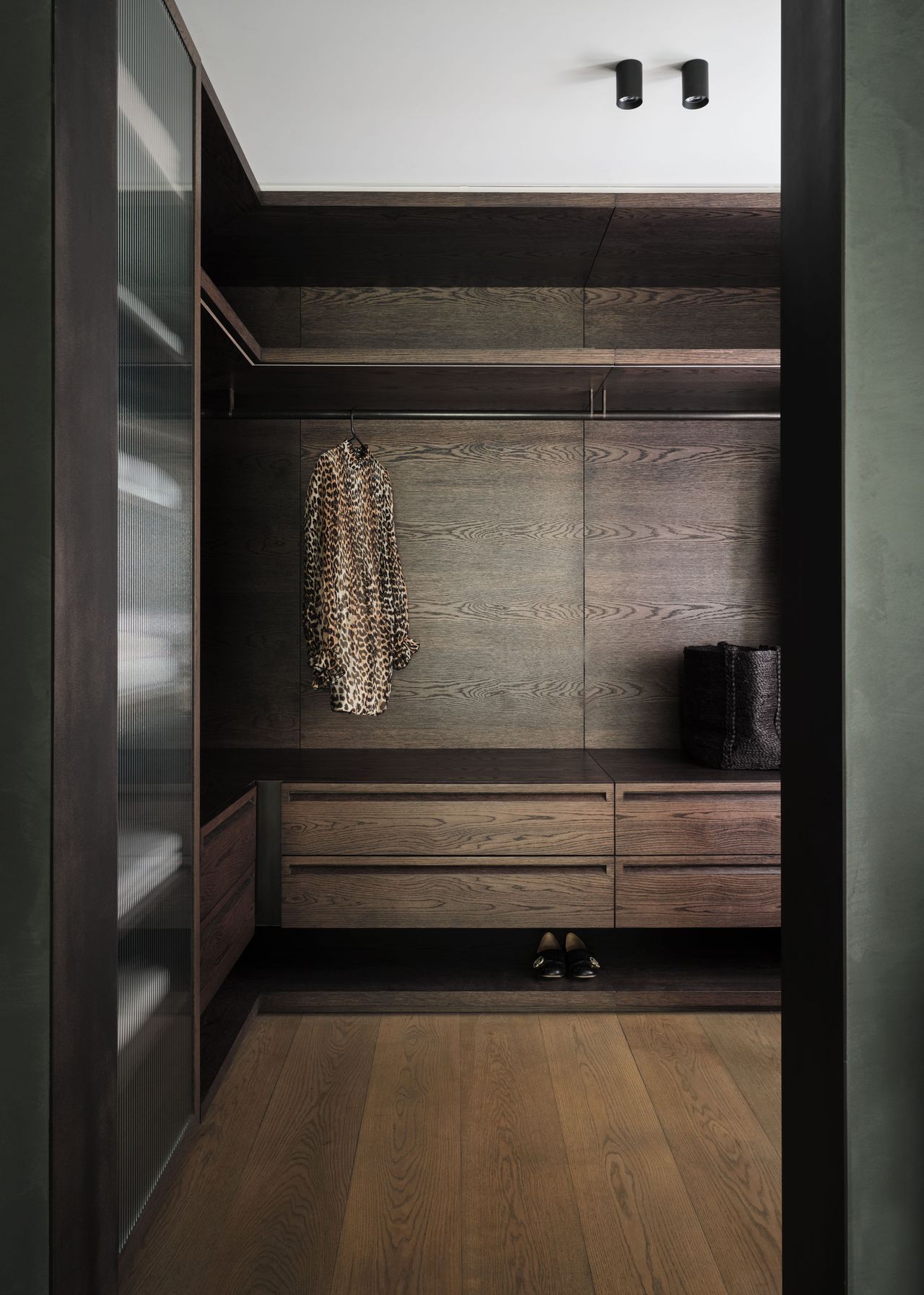 Custom walk-in wardrobe with dark timber cabinetry, integrated drawers, open hanging space and fluted glass doors.