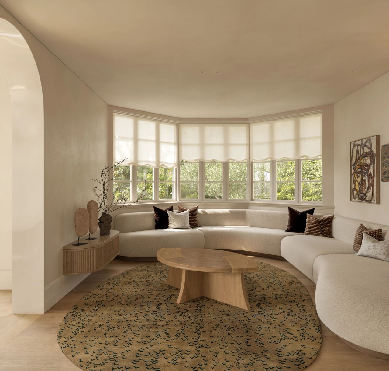 Lady M TV room with a curved cream boucle sectional sofa wrapping a bay window, styled with velvet and patterned cushions. A round timber coffee table sits on a patterned wool rug, with a fluted timber console, sculptural objects, and framed artwork completing the space, lit by soft garden views through the windows.