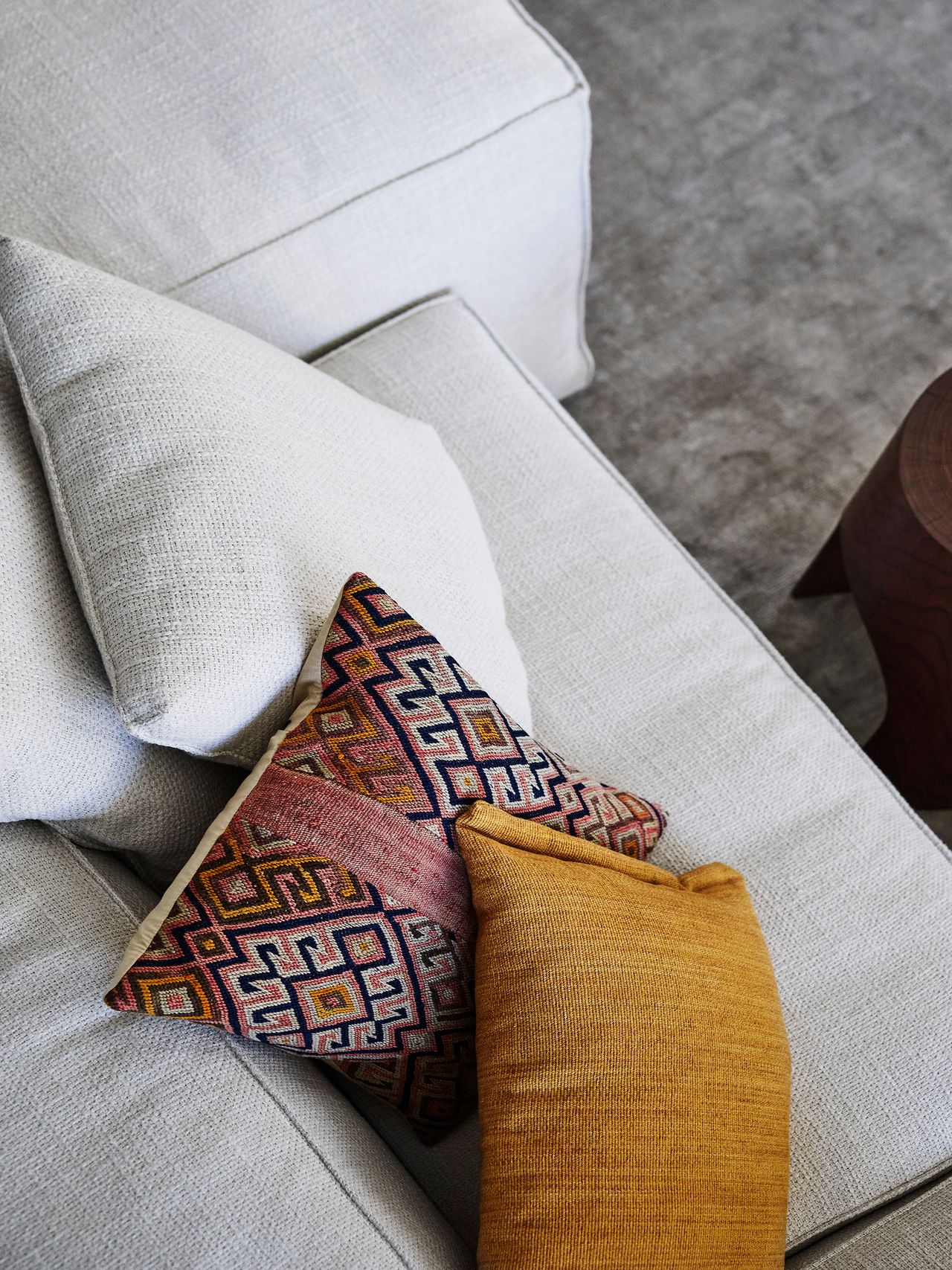 Patterned and mustard cushions bring warmth and character to a softly textured neutral sofa, reflecting the home's playful mix of colour, pattern and relaxed luxury.