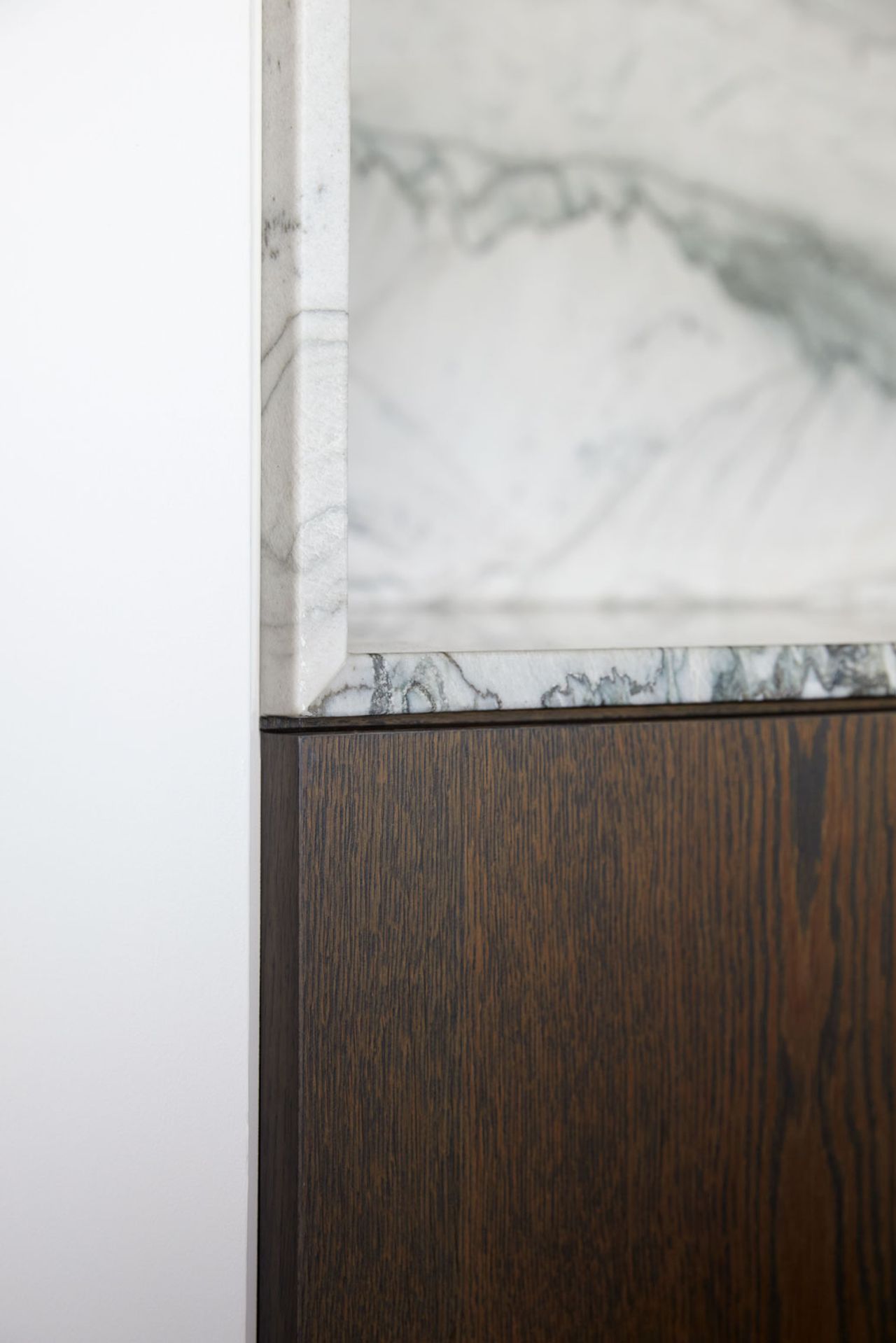 Detail of richly veined white marble and dark timber cabinetry in a contemporary kitchen.