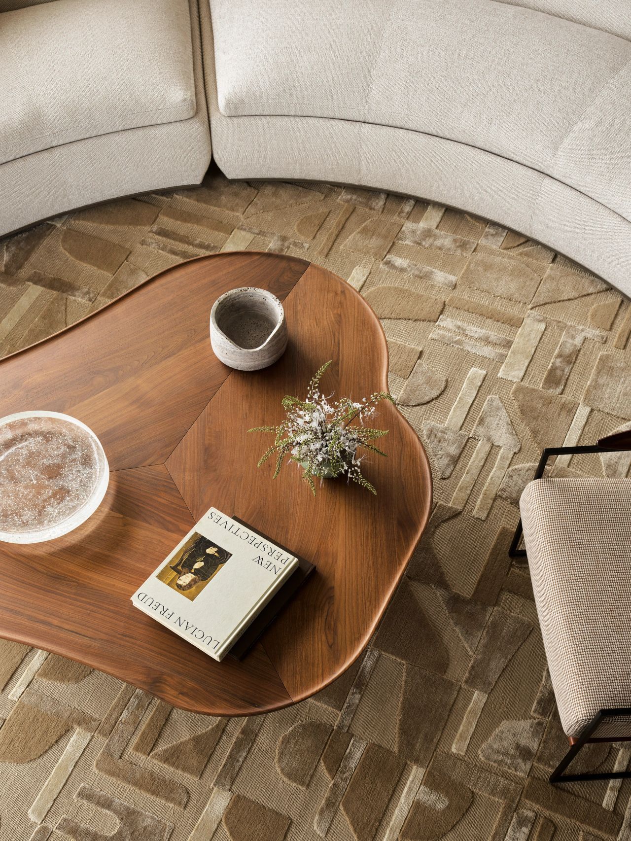 Orla contemporary open-plan living room blending Brazilian influences, with a walnut coffee table on cream-glazed ceramic legs beside a Brazilian-style occasional chair with beige upholstery and timber arm detailing, both sitting on a cream geometric-patterned rug.