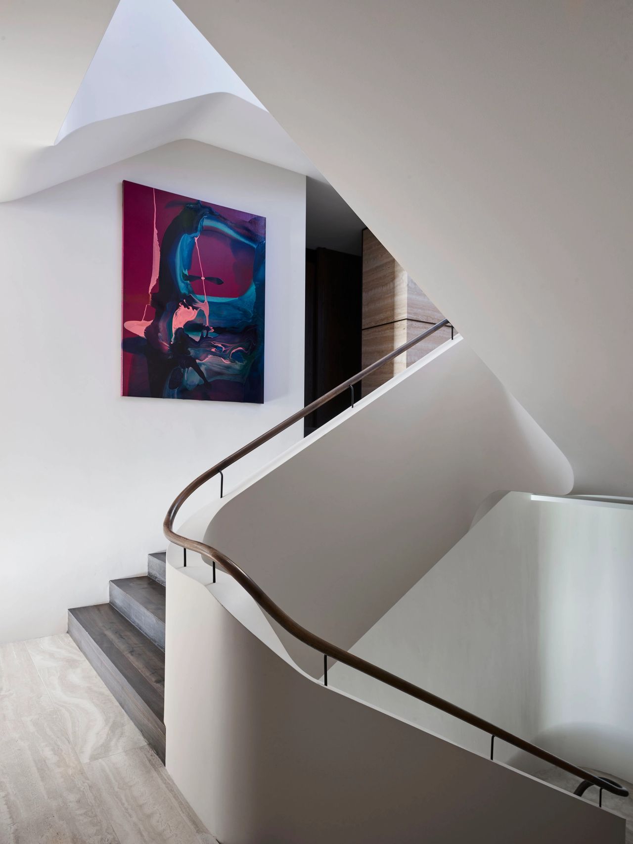Sculptural curved staircase with a dark timber handrail, white walls and vibrant abstract artwork in a contemporary interior.