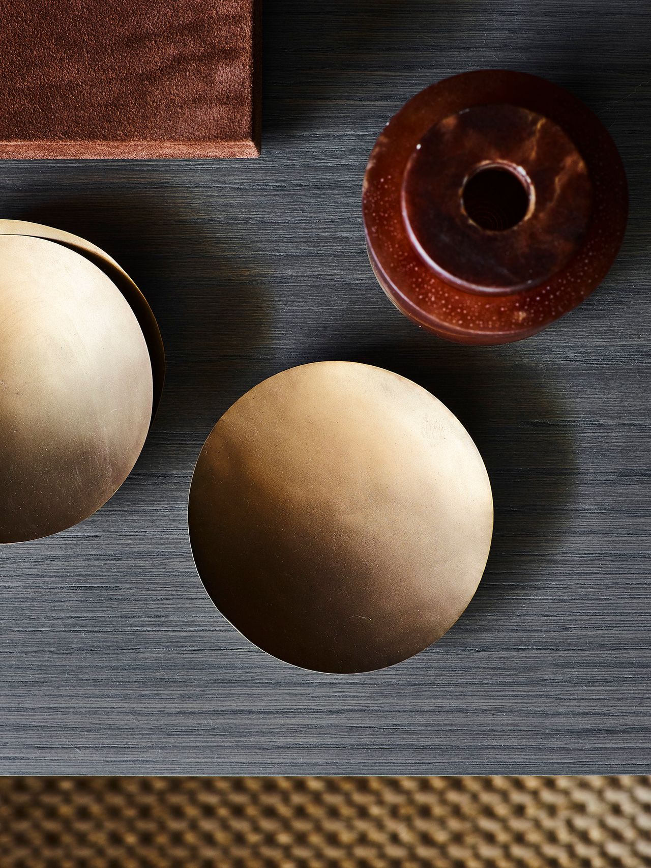 Killcare Overhead detail of round brass coasters and a small red marble vessel styled on a brushed grey timber surface