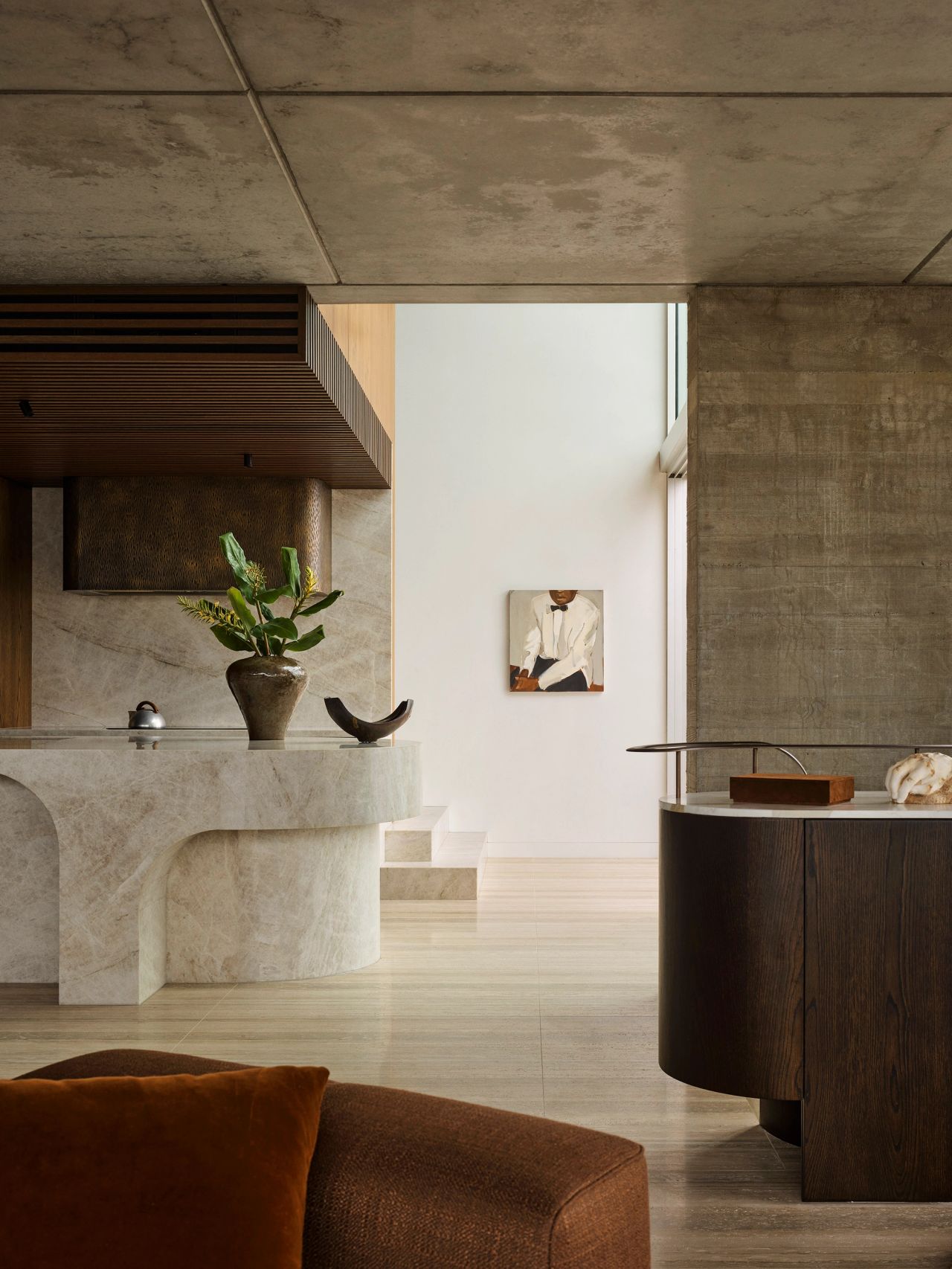 Orla Contemporary open plan living room and kitchen blending Brazilian influences with a warm brown, black, and camel palette; Large white beige quartzite granite kitchen island, looking through to small artwork of a man in a white tuxedo