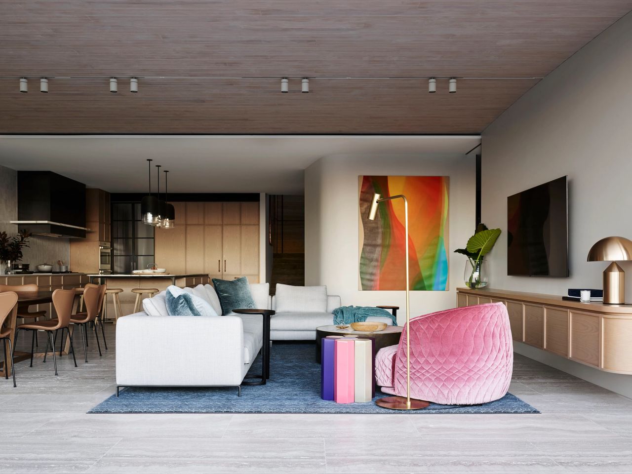 Hill House living room, stone coloured sofa, pink velvet armchair in the foreground with colourful artwork and travertine floors