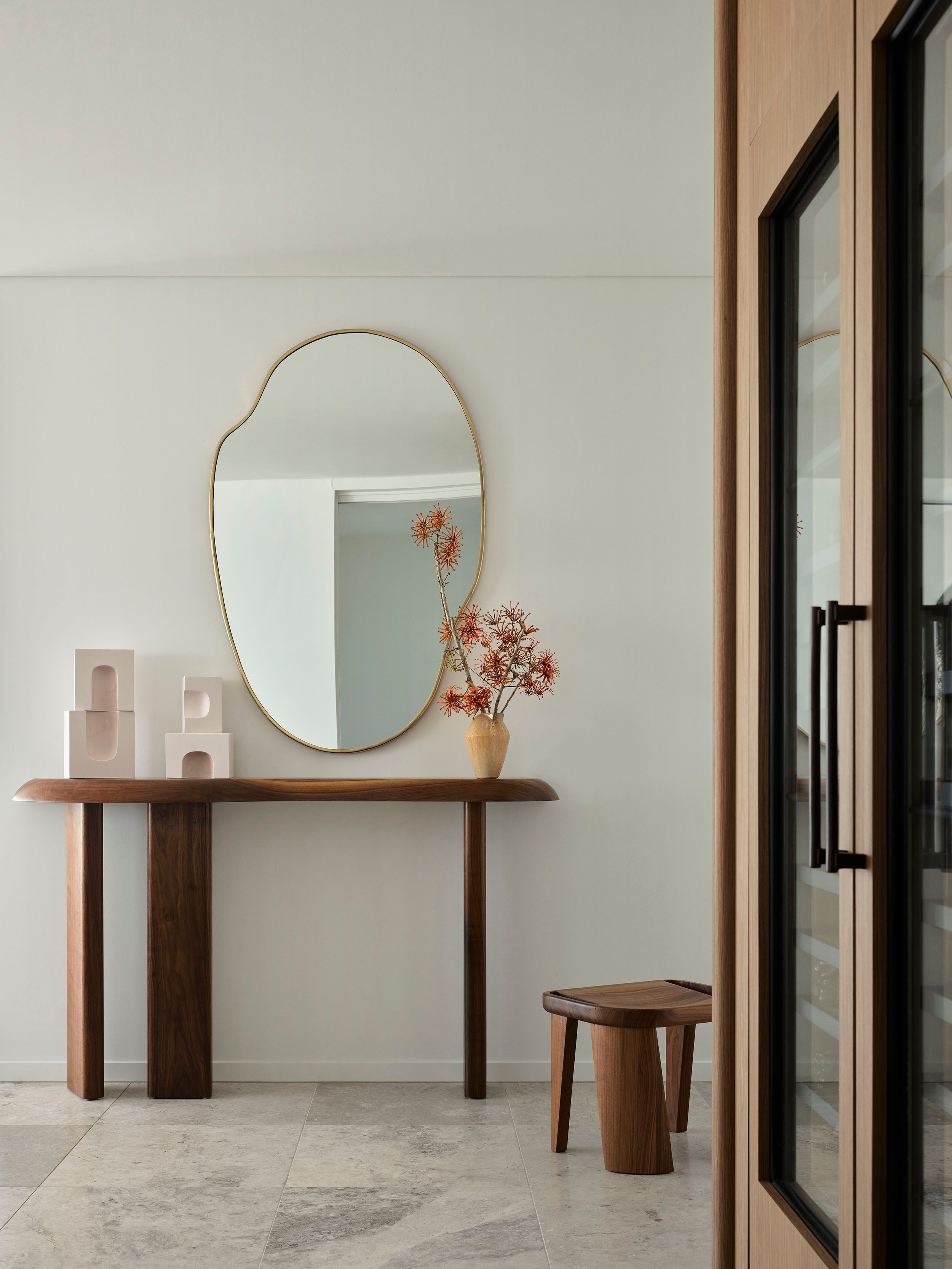 Sculptural timber furniture and an organic brass-framed mirror create a refine entry moment in the penthouse by Decus