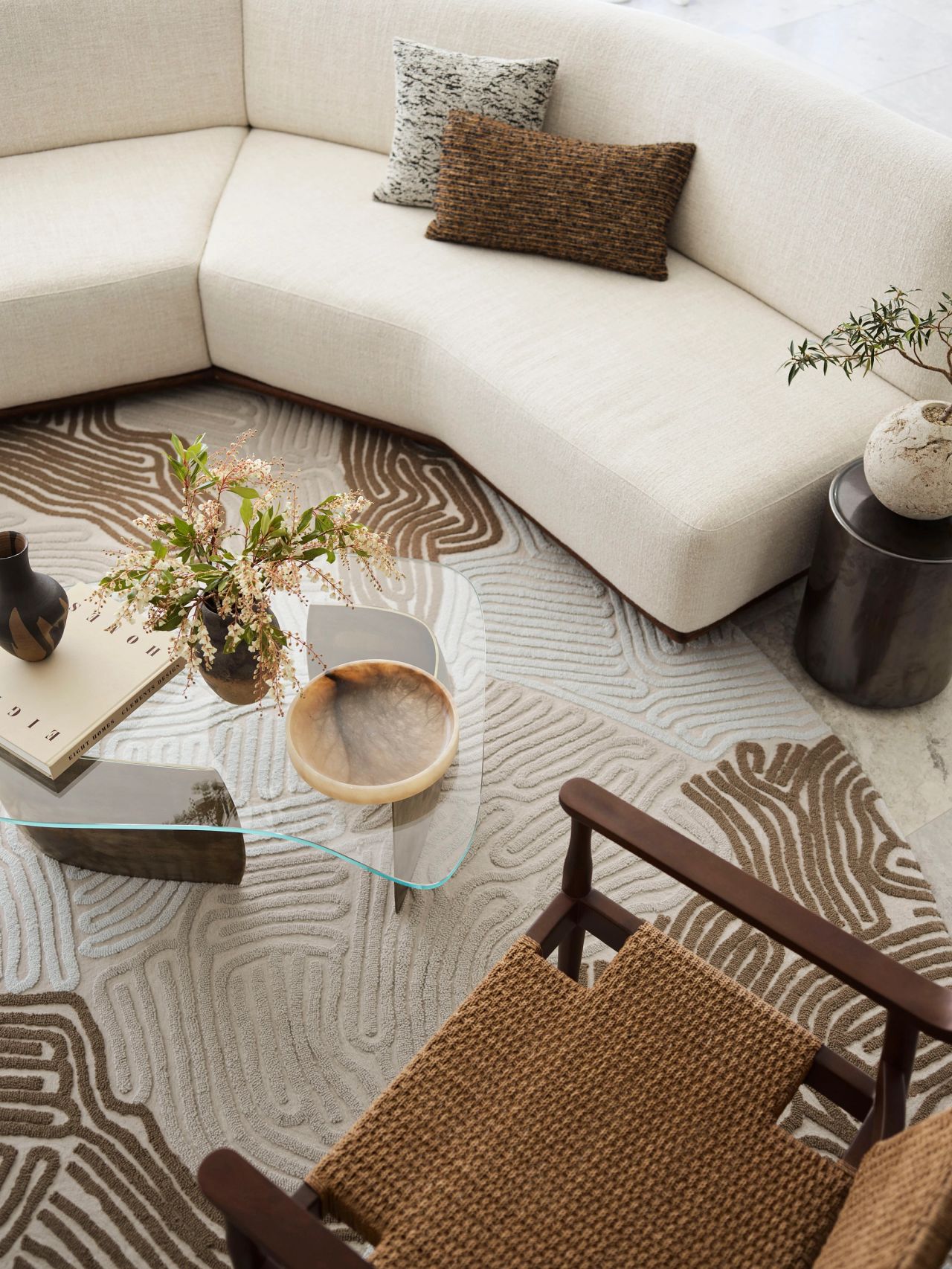 Cloud Surfer living room by Sydney interior design studio Decus, featuring a curved cream sofa, patterned rug, woven armchair and sculptural glass coffee table.