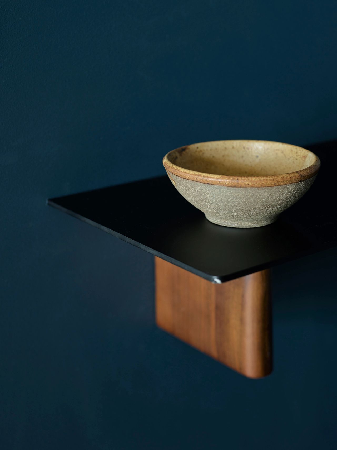 A handcrafted ceramic bowl is displayed on a wall-hung shelf, against deep ocean-blue walls.