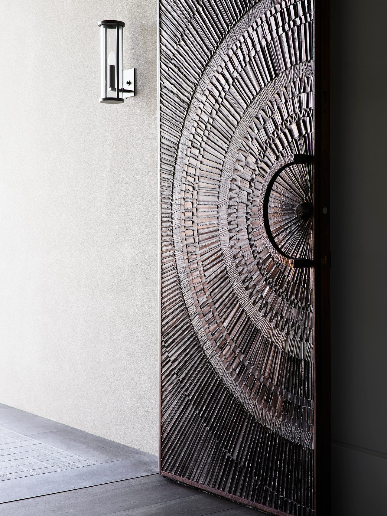An intricately detailed sculptural entrance door creates a dramatic contemporary arrival at this heritage coastal home by Sydney interior design studio Decus.