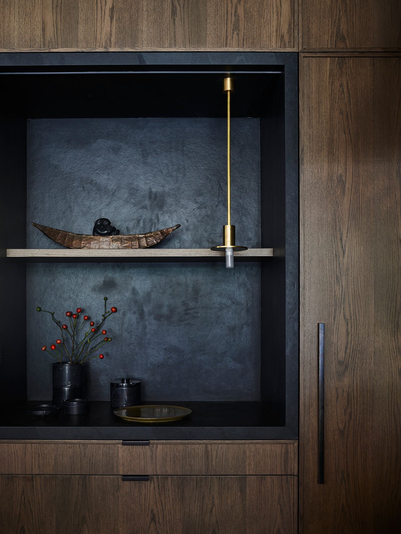 Dark timber joinery frames a moody display niche styled with sculptural objects, highlighting the kitchen's rich material palette.