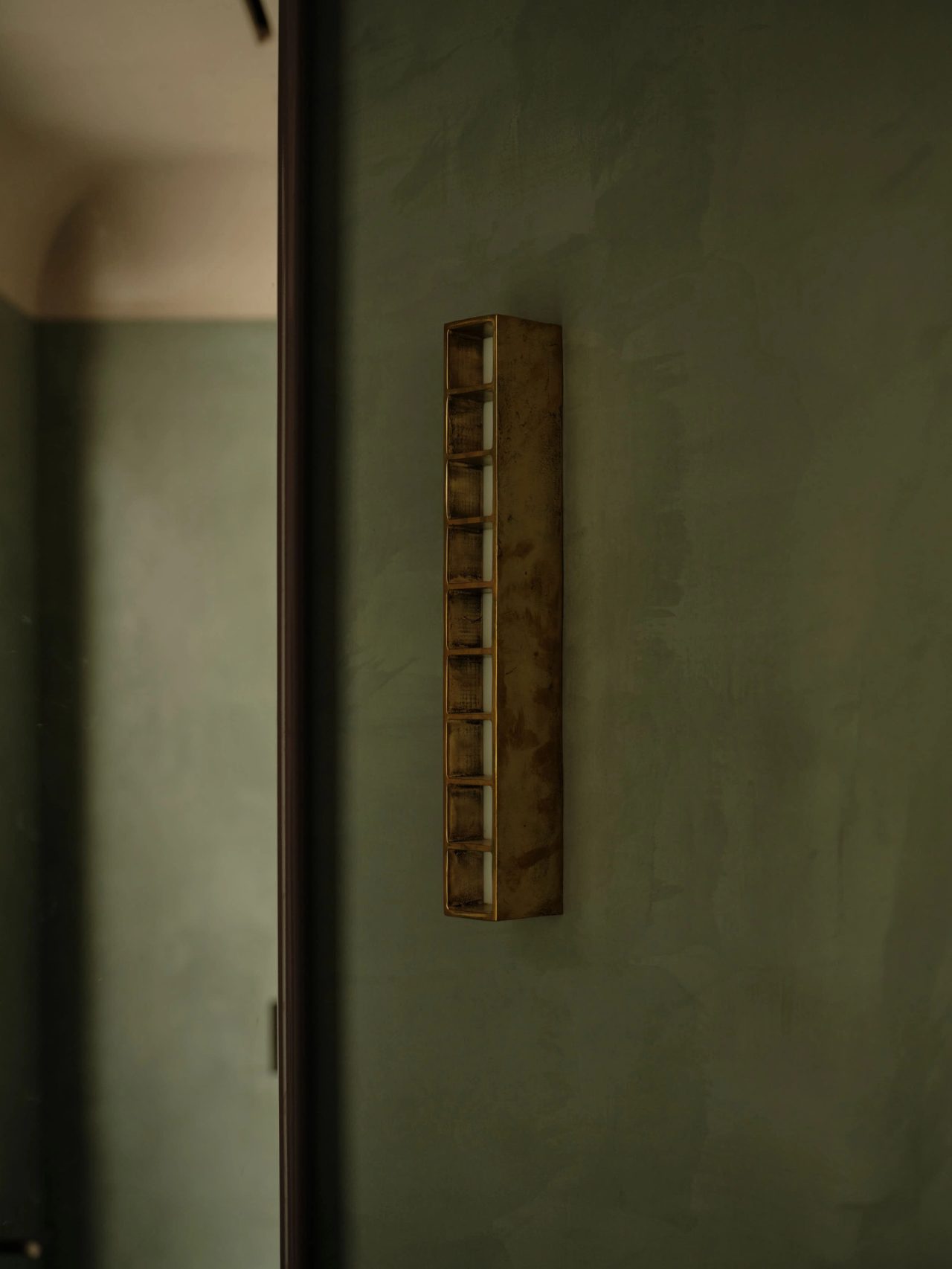 Sunset, powder room detail sage-green plaster walls, beneath a slim rectangular mirror and a ridged wall sconce