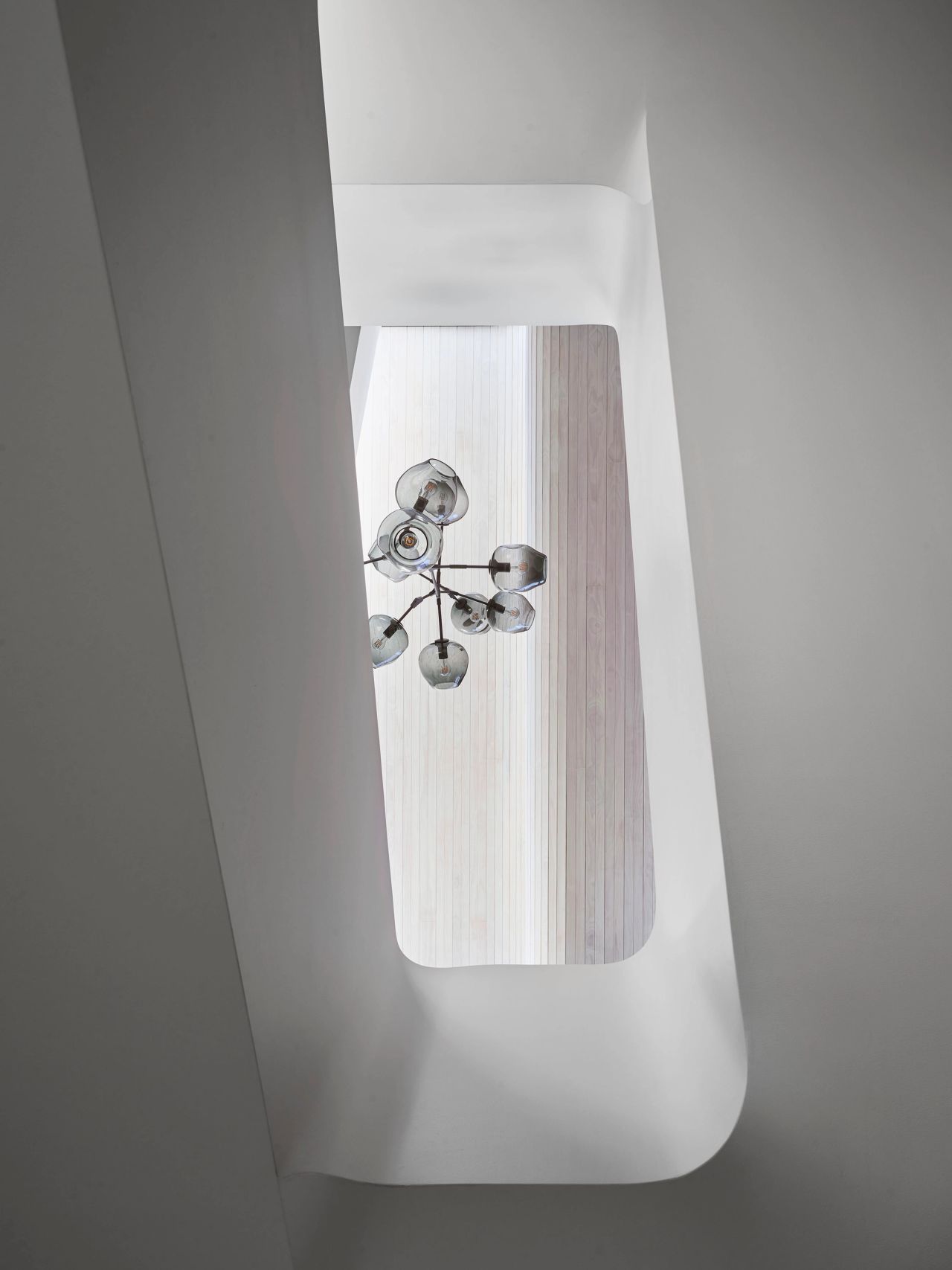Sculptural white stairwell with curved architectural forms, a skylight and contemporary glass globe chandelier.